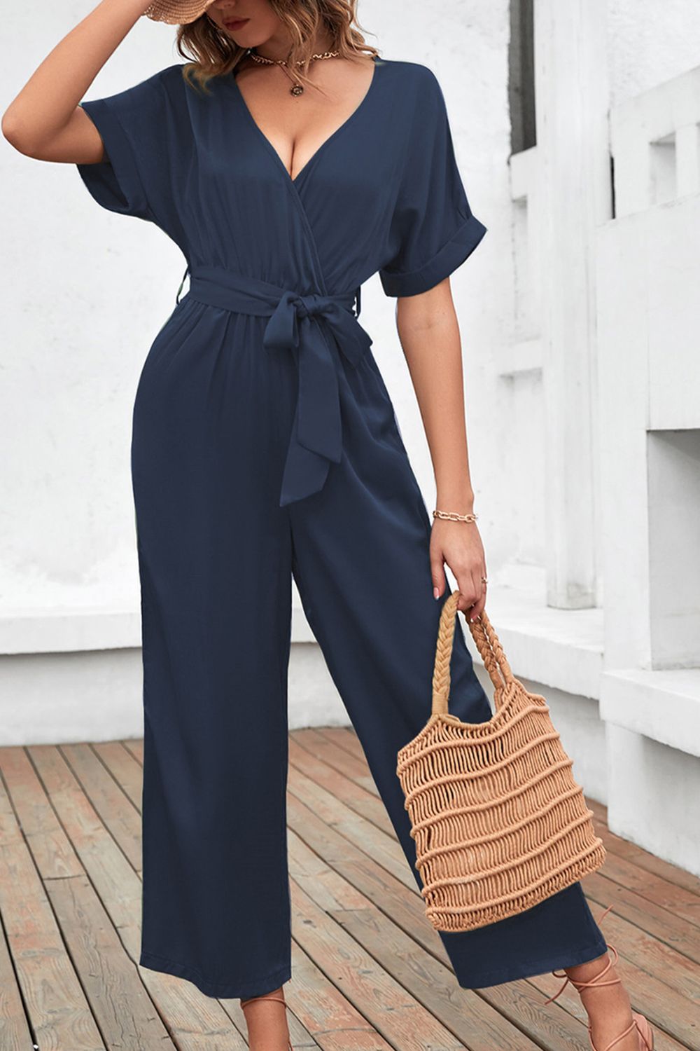 Women's navy short-sleeve jumpsuit with a surplice neckline, tied waist, and wide legs.