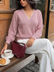 Seated front view of a pink V neck sweater with white trim and openwork chevron long sleeves.