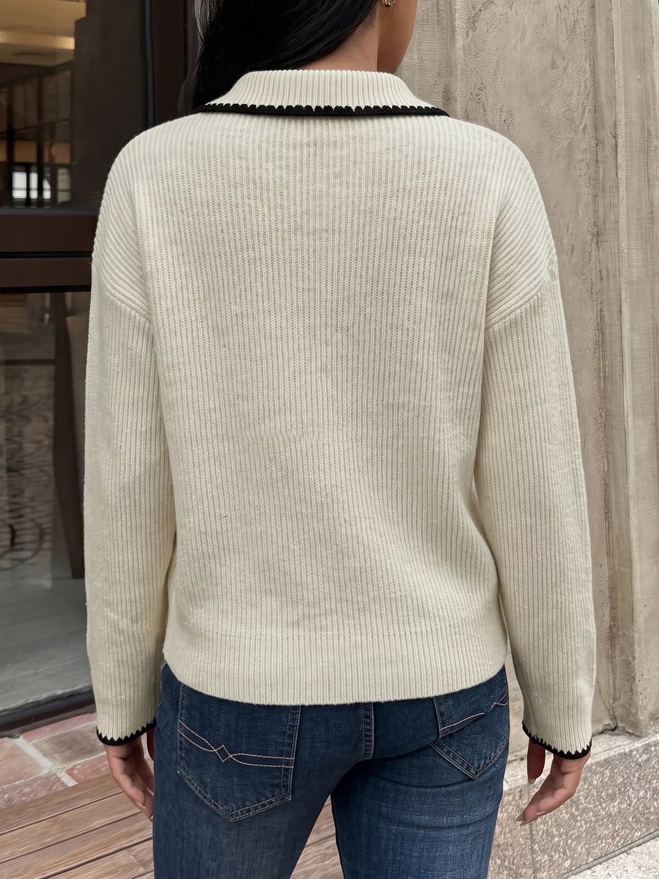 Back view of a plain cream ribbed sweater with black scalloped collar and cuff trim