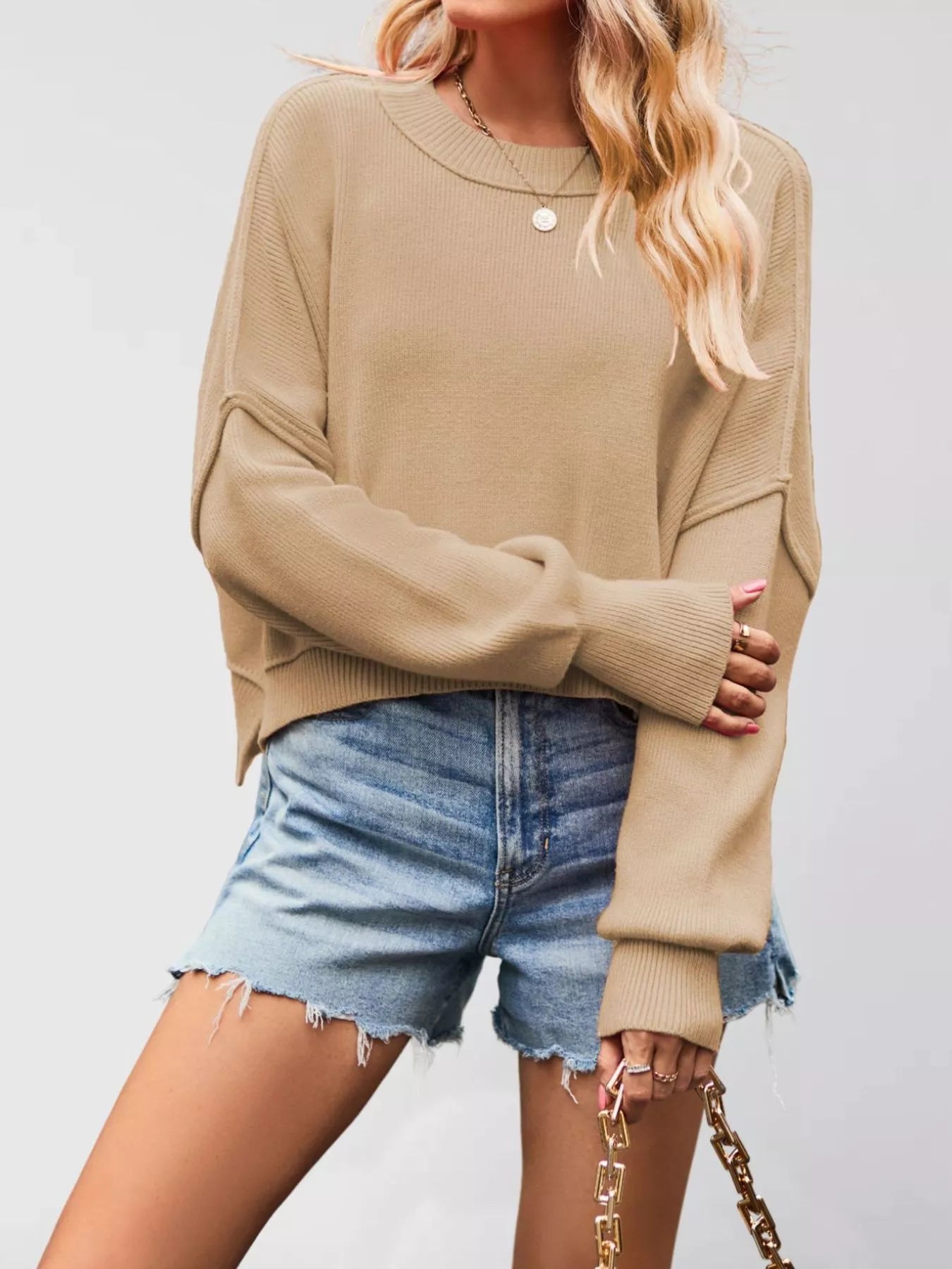 Front view of a khaki crew neck dropped shoulder sweater with ribbed cuffs worn with denim shorts.