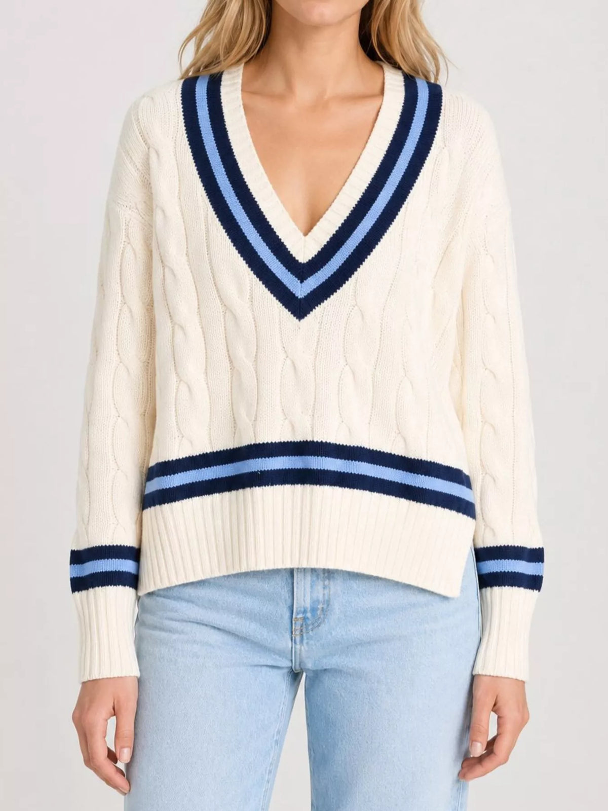 On-model front view of a cream cable knit sweater with navy and light blue striped trim