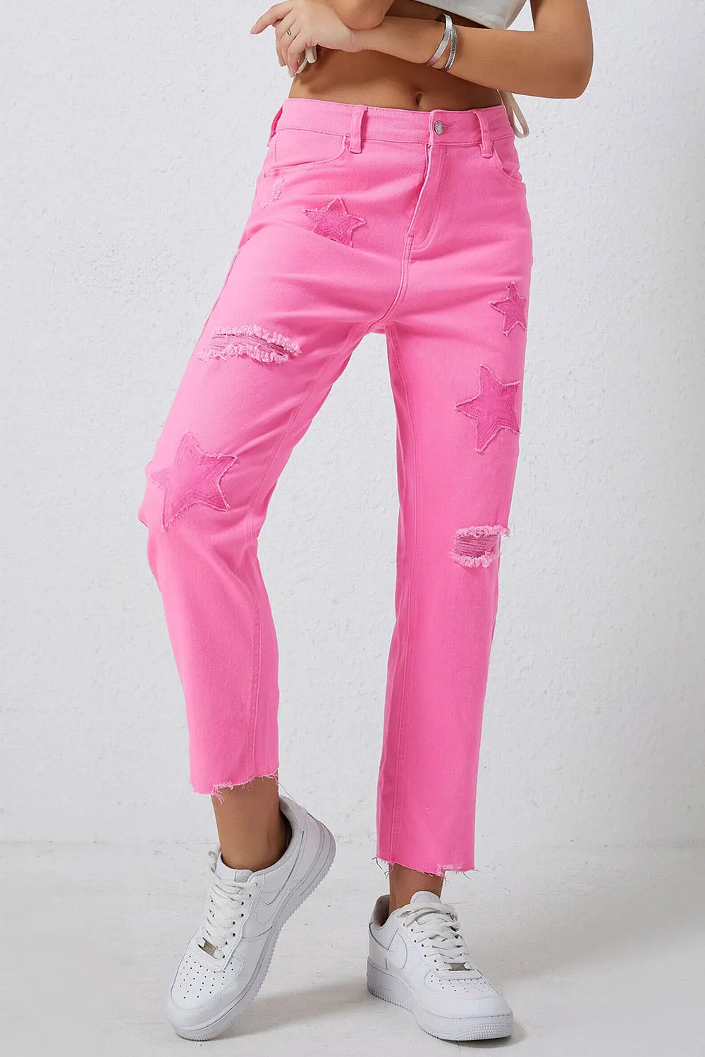 Women's pink jeans with star detailing, distressed areas, and raw hems.