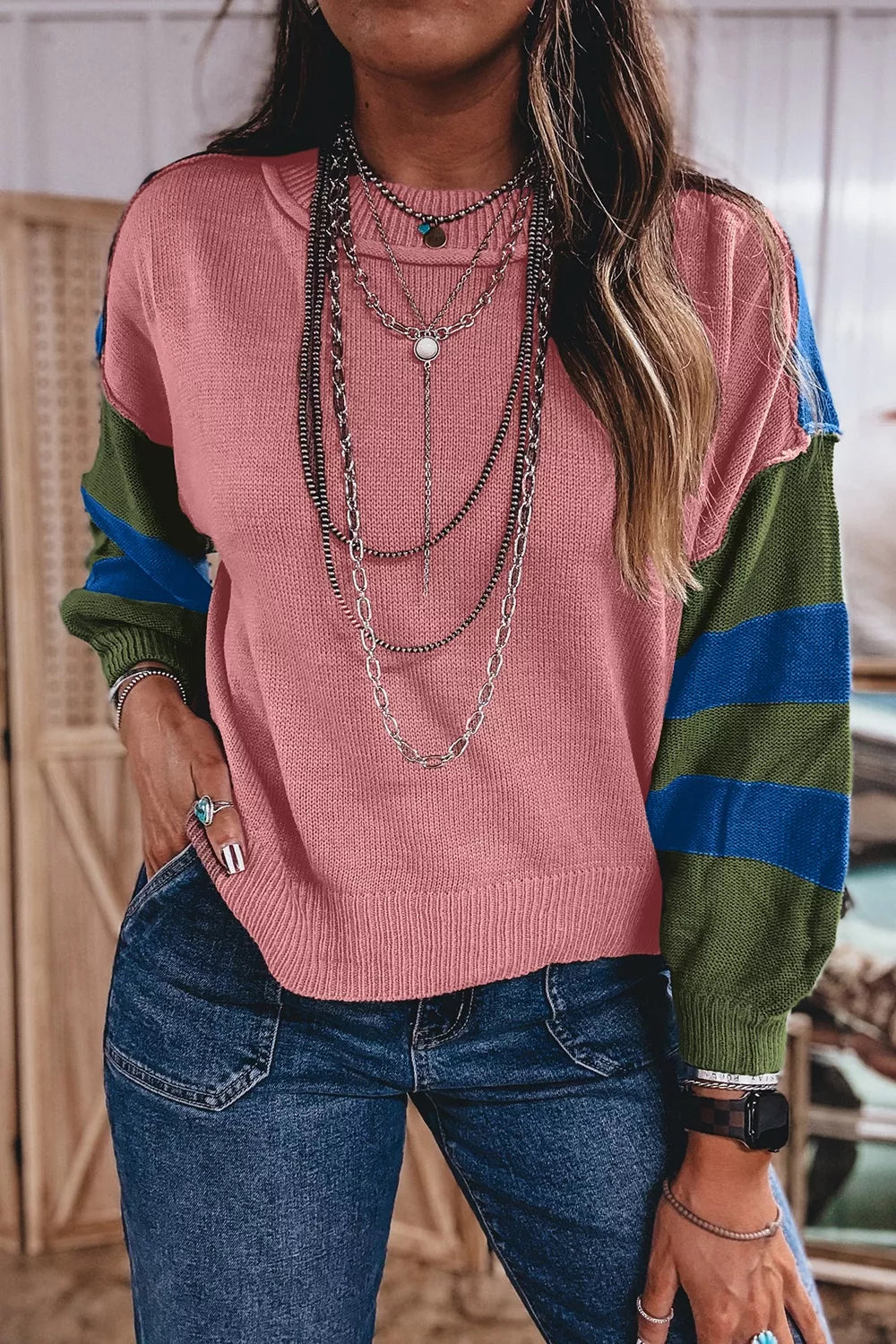Close torso view of a dusty pink sweater with green and blue striped sleeves