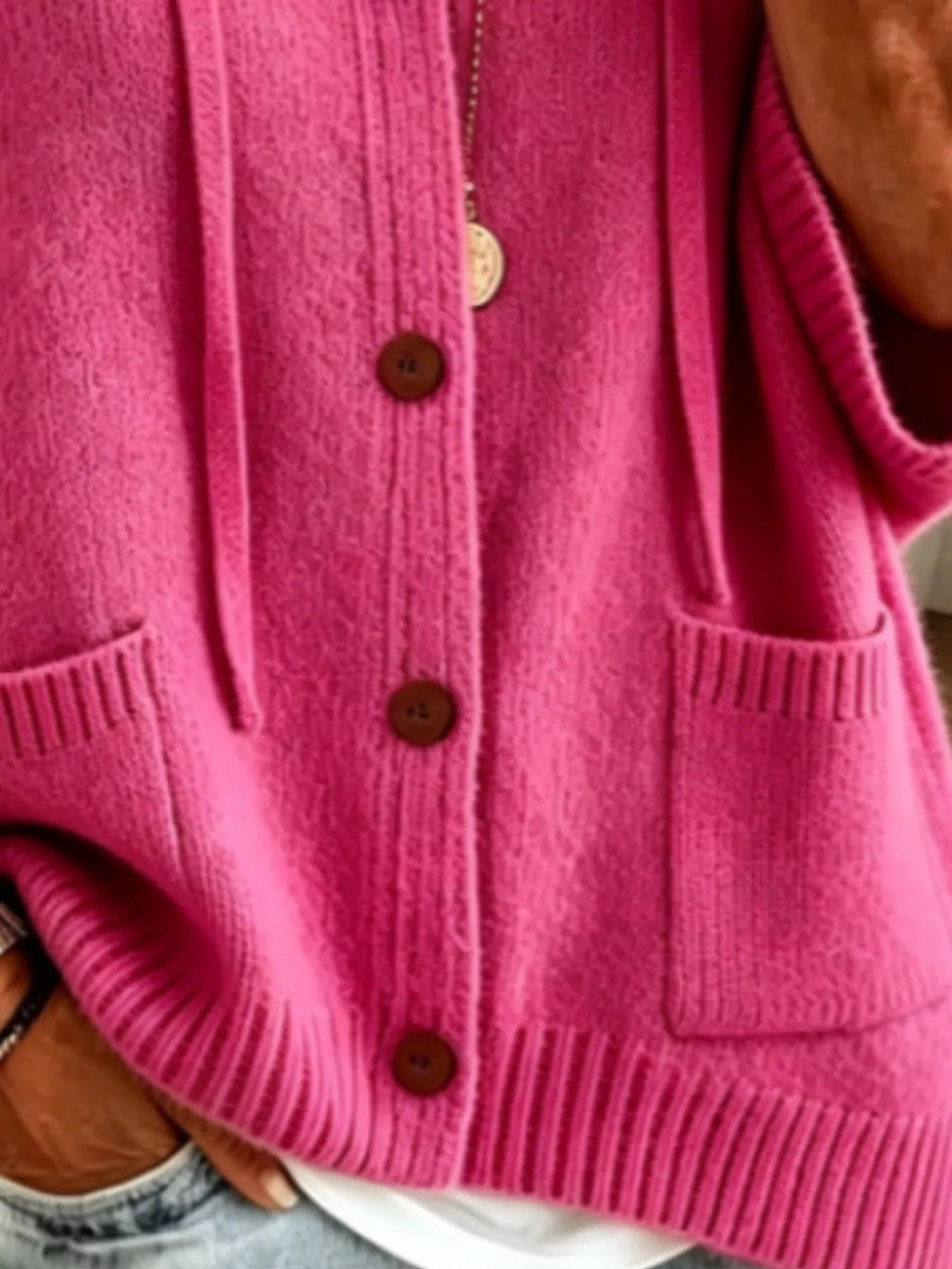 Detail view of the fuchsia pink cardigan showing brown buttons, patch pockets and ribbed hem