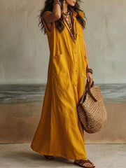 Gold sleeveless button down linen maxi dress shown from the side while holding a woven bag