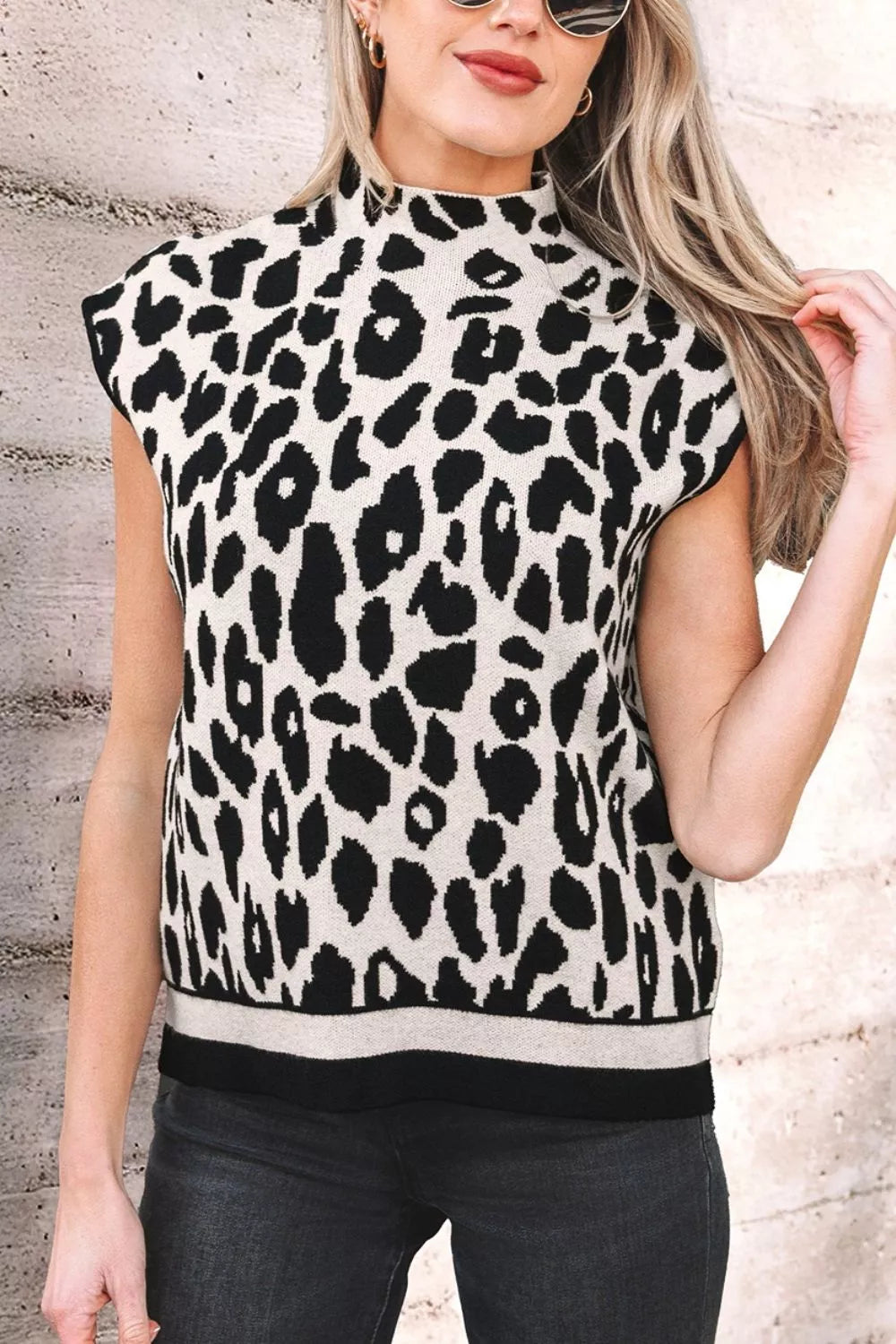 Close front view of the black and cream leopard print high neck sweater with cap sleeves, outdoors.
