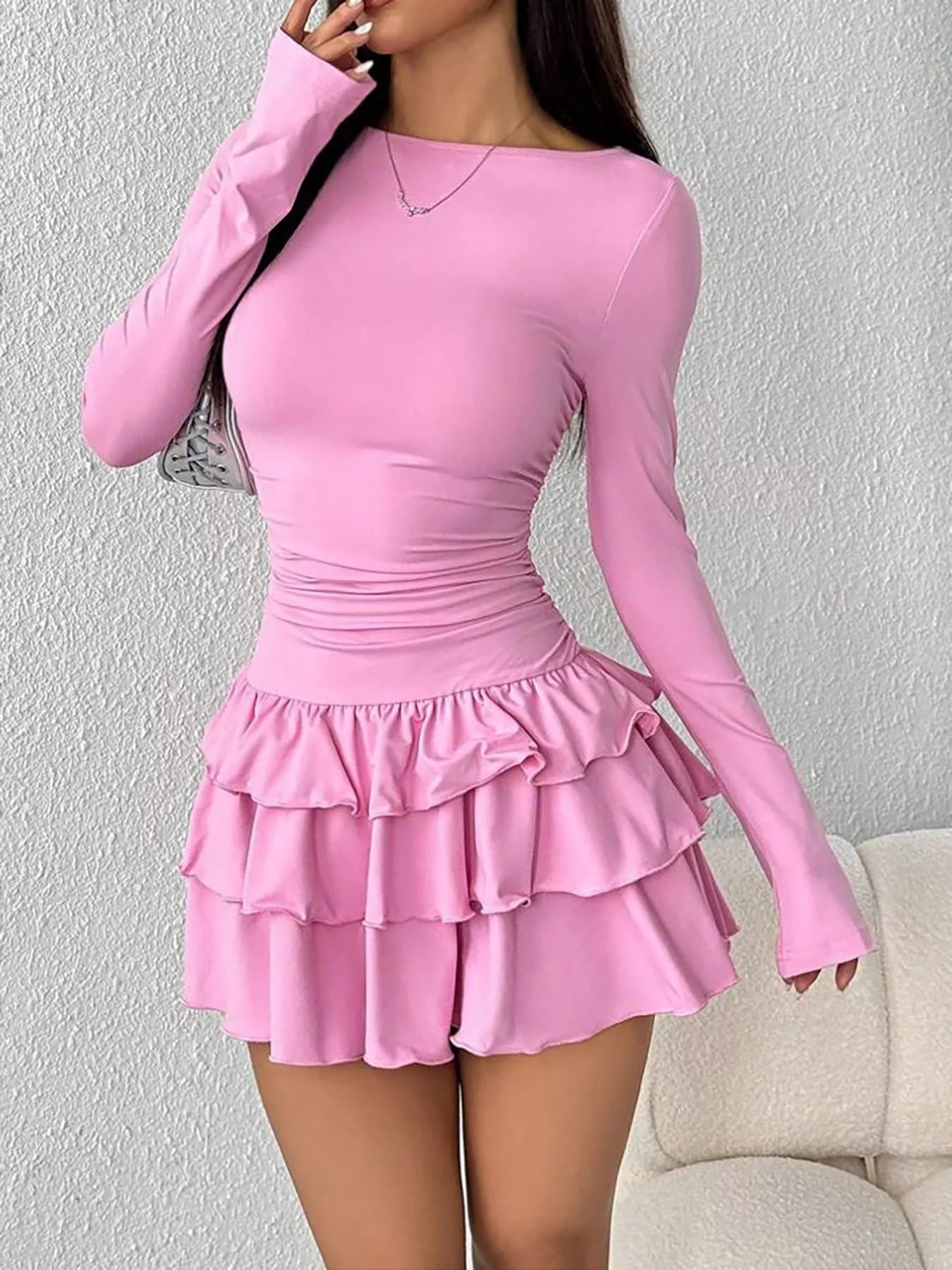 Pink long sleeve mini dress worn front facing with one hand raised near the face