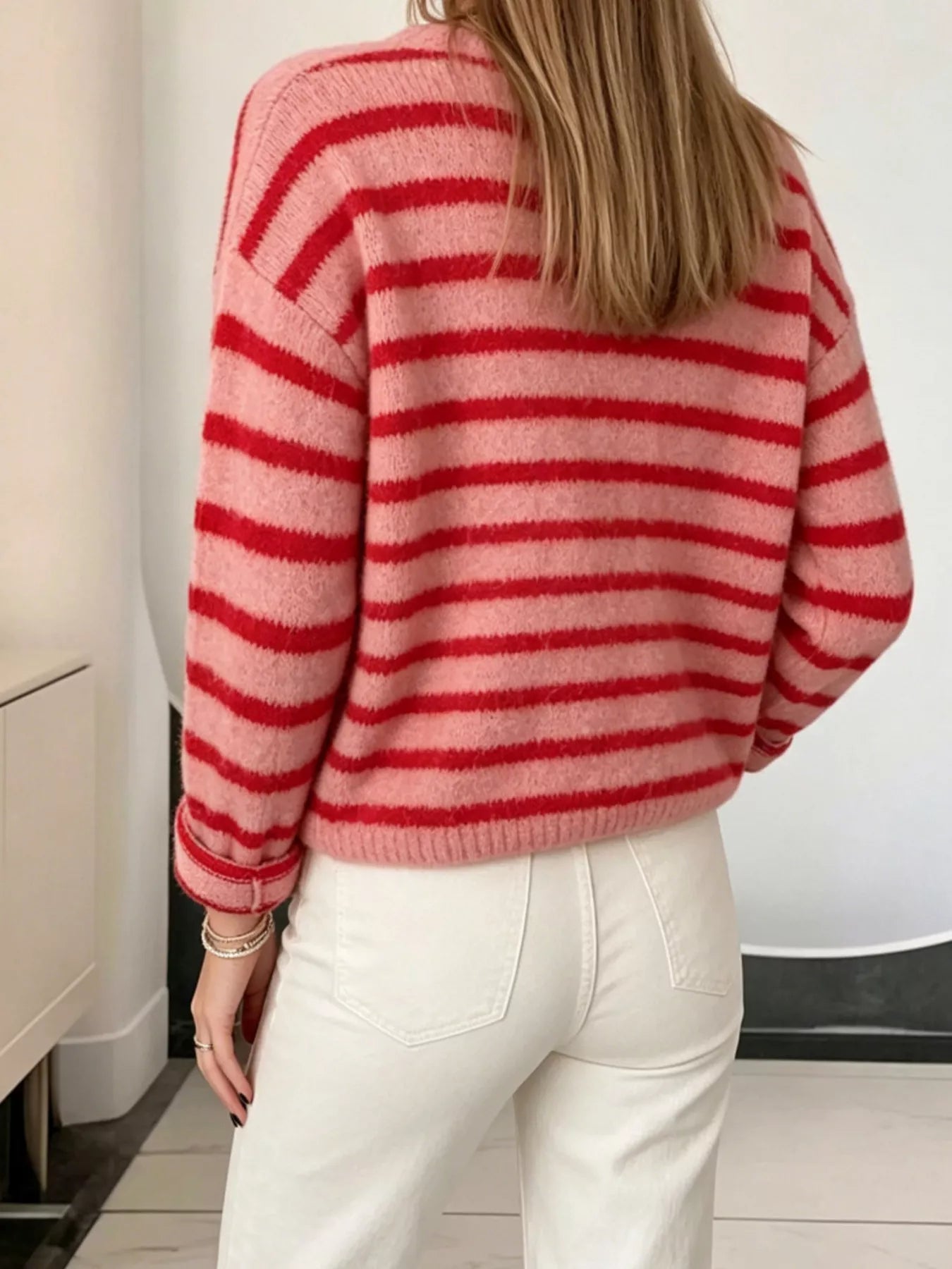 Back view of pink and red striped button down cardigan with long sleeves and white pants