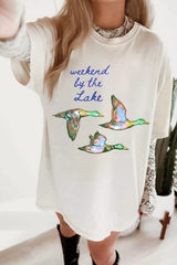 White oversized T-shirt featuring blue “weekend by the Lake” lettering and three colorful flying ducks.