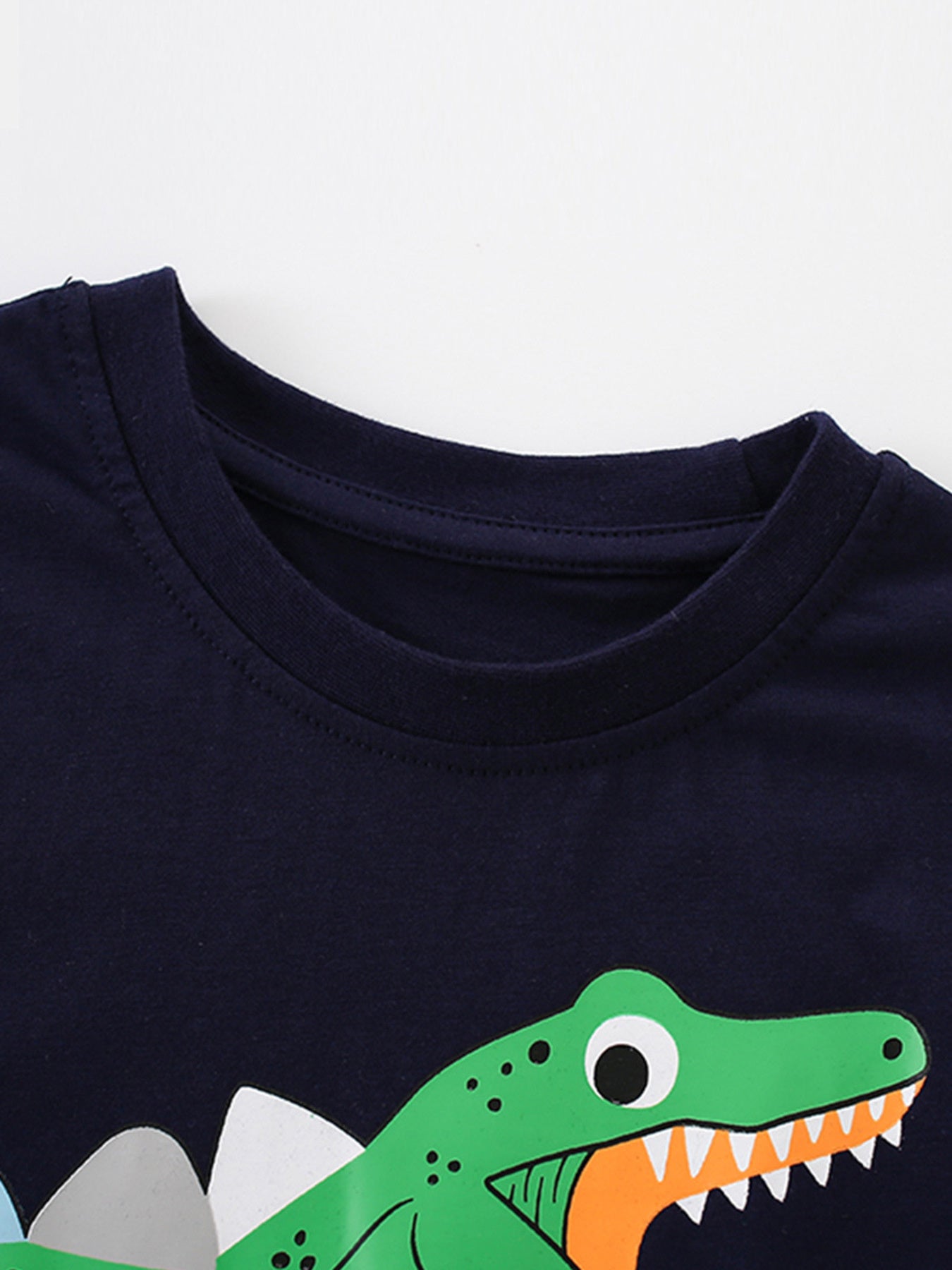 Close-up of the black round neckline and green dinosaur head graphic on a children's T-shirt