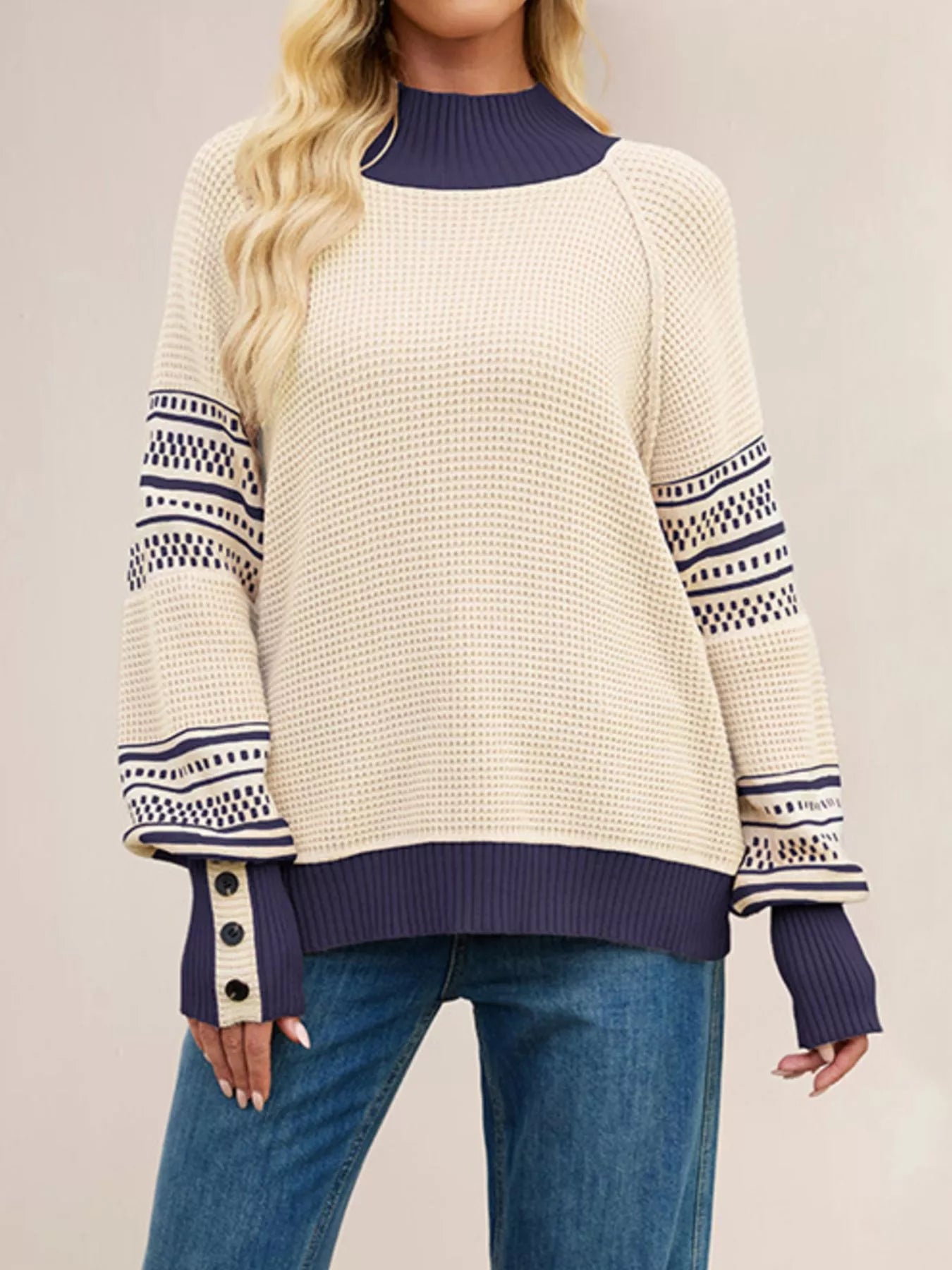 Front view of a cream waffle knit sweater with navy mock neck, patterned sleeves, and button cuffs.