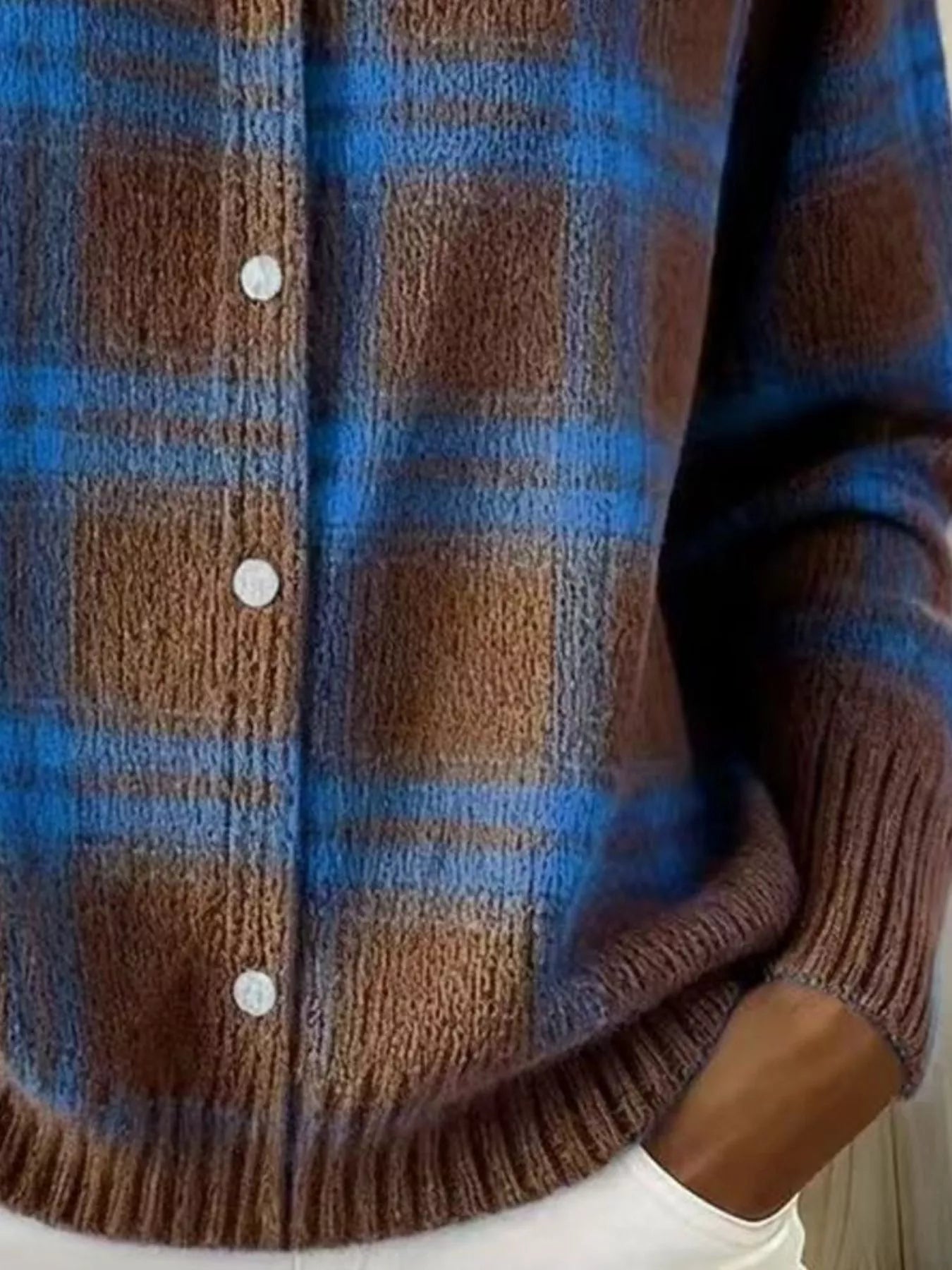 Close-up of the lower front and ribbed hem of a brown and blue plaid knit cardigan