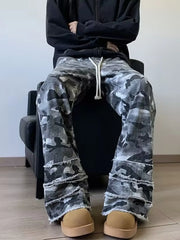 Men's grey camouflage wide leg jeans with white drawstrings and frayed hems, seated on model.