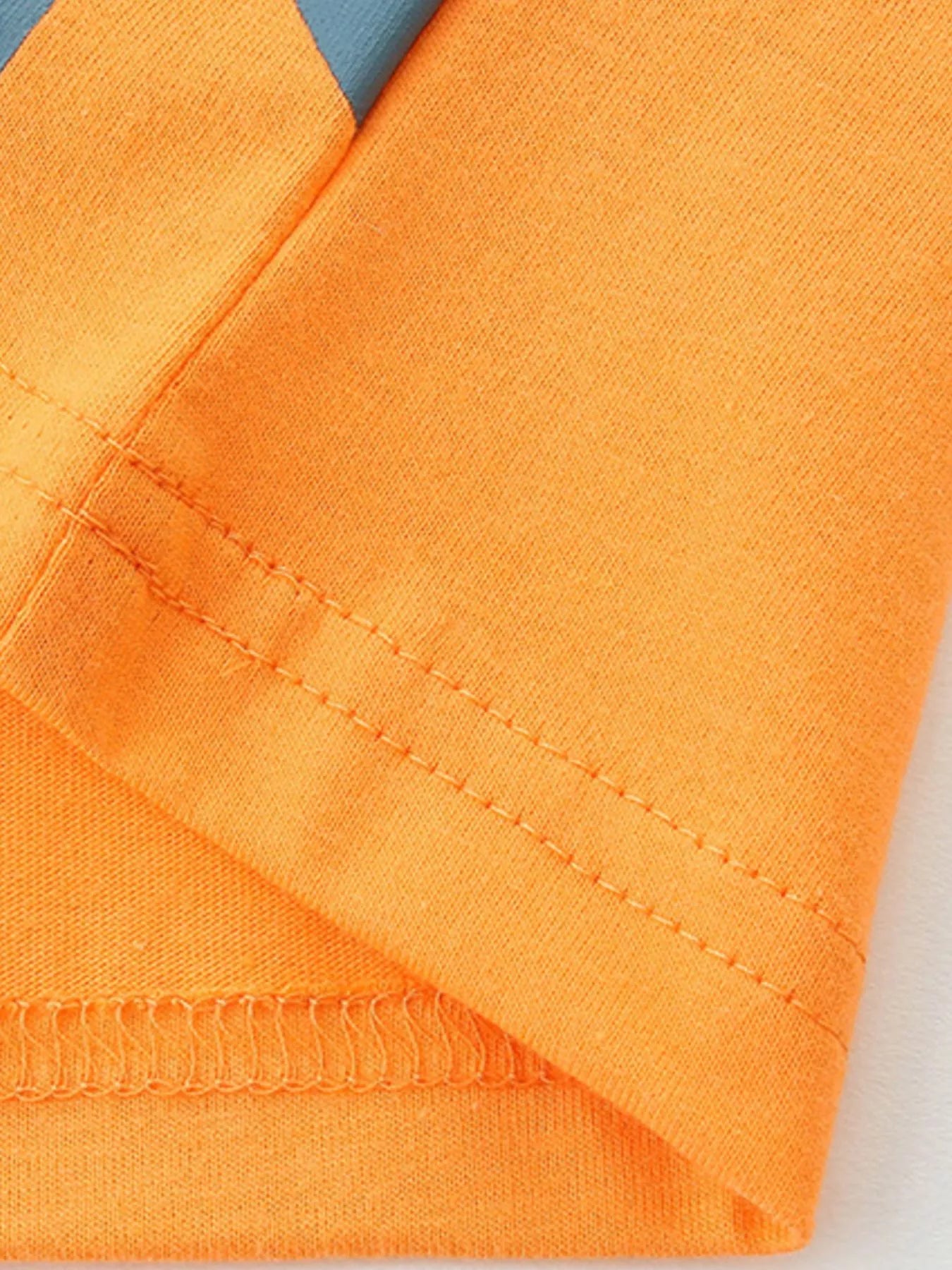 Close-up of orange tee hem and sleeve stitching showing neat double seams and fabric texture
