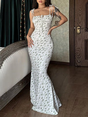 Model standing indoors in white floral print bodycon maxi dress with tie shoulder straps and front tie