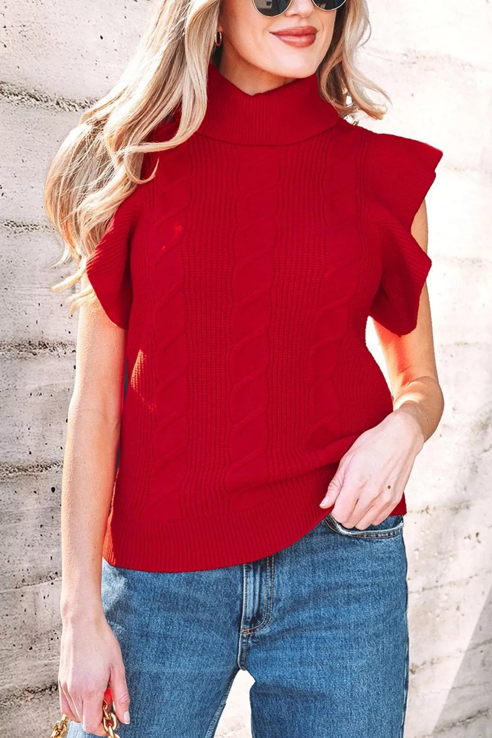 Outdoor front view of a red cable knit turtleneck sweater with ruffled short sleeves