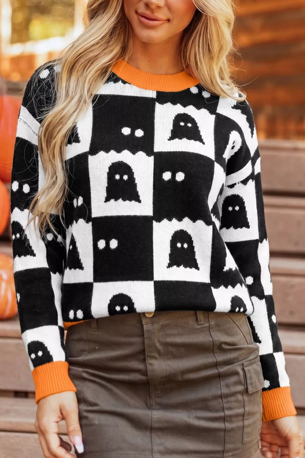 Front view of a ghost checkerboard sweater with orange trim, worn with a brown skirt