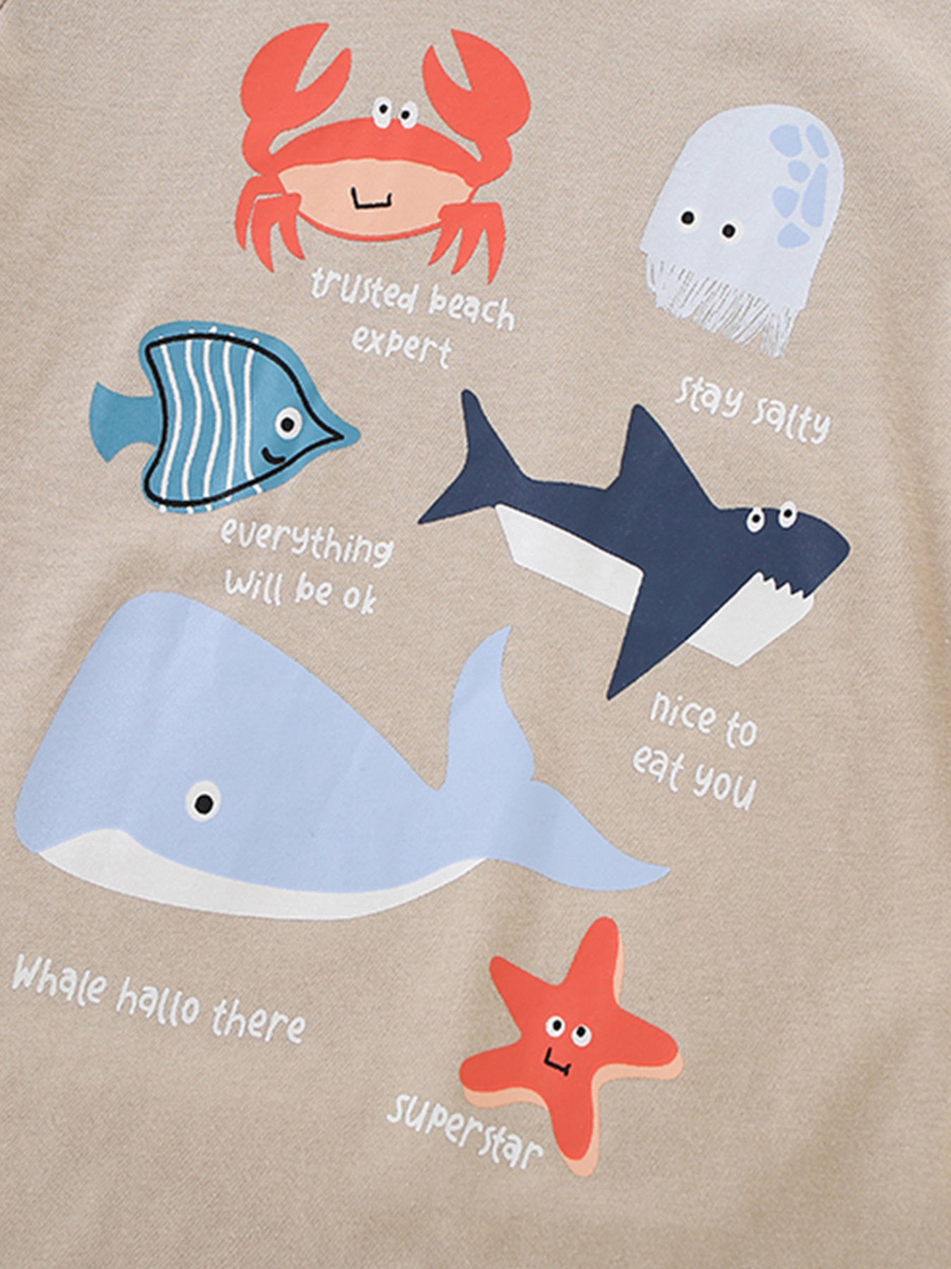 Close-up of the crab, shark, whale and starfish graphics on a tan children's short sleeve tee