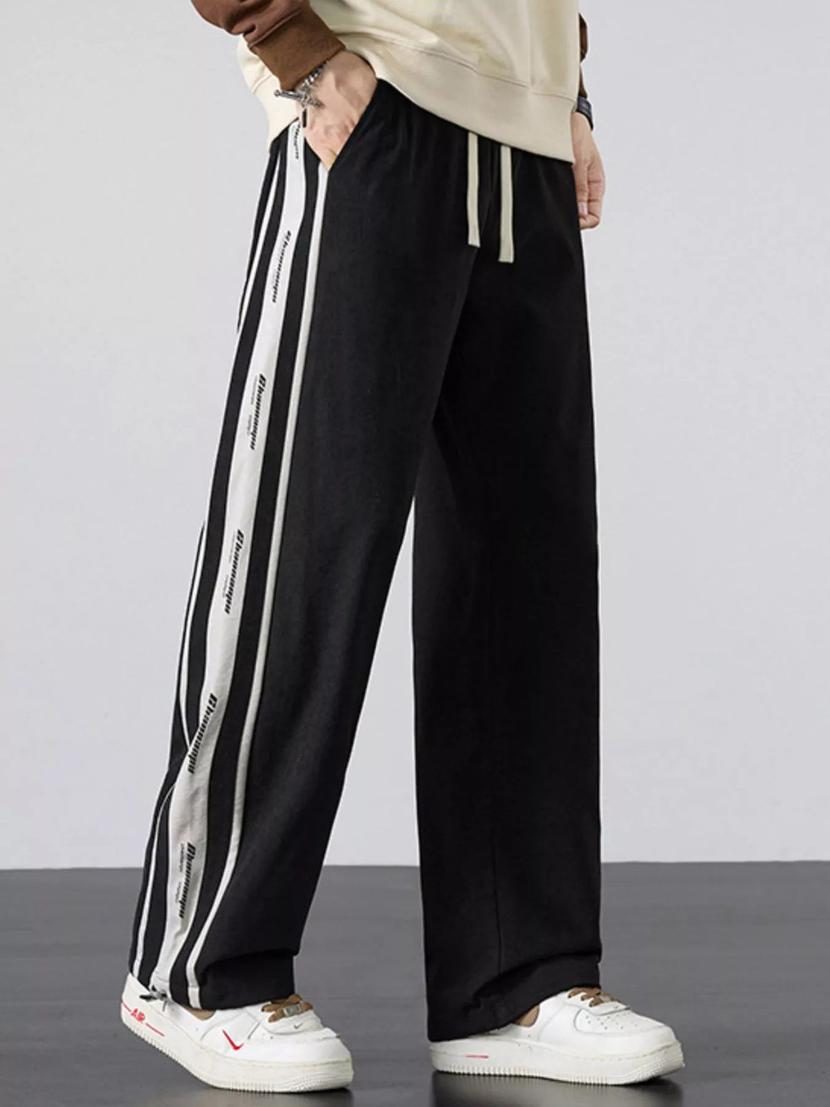 Men's black loose-fit pants with side stripes and a drawstring waist.