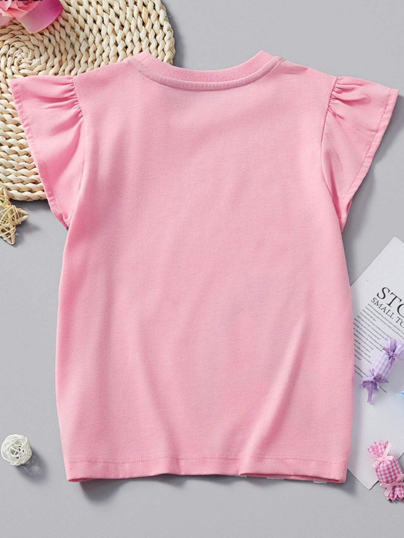 Flat back view of a plain blush pink children's ruffle sleeve tee laid on gray surface