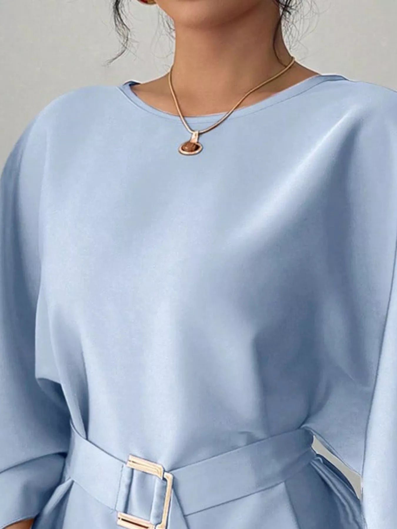Close view of light blue round neck blouse showing neckline and gold buckle belt