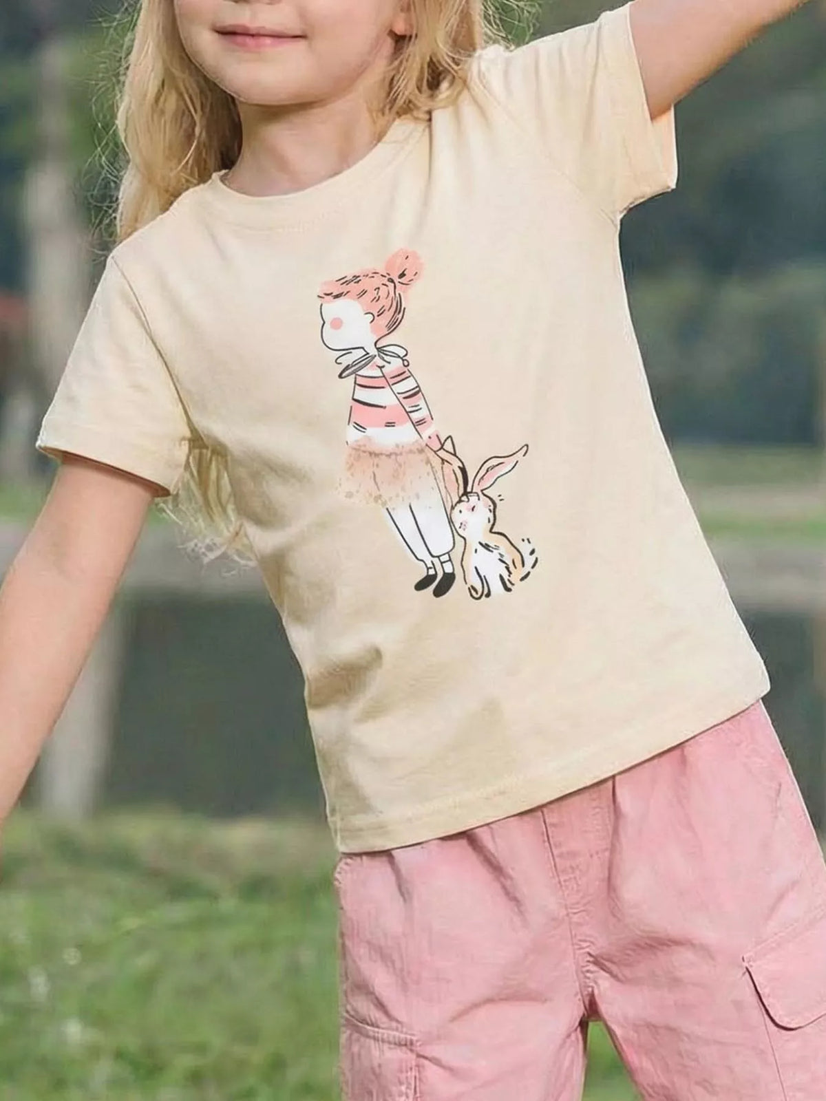 Cream children's short sleeve T-shirt shown worn outdoors with a striped top and rabbit graphic on the front