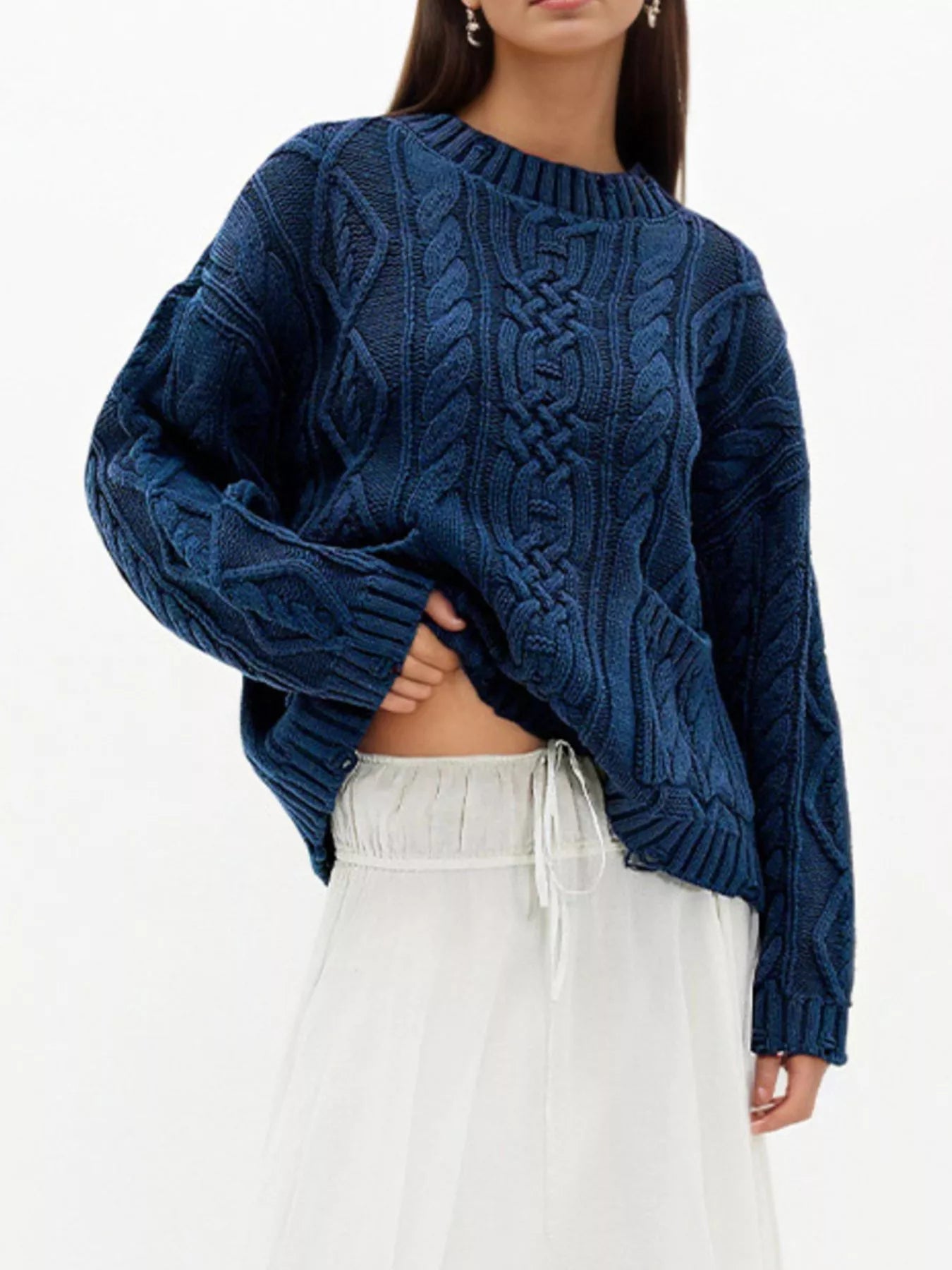 Front view of blue cable knit sweater with front pockets and white skirt with hand at hem