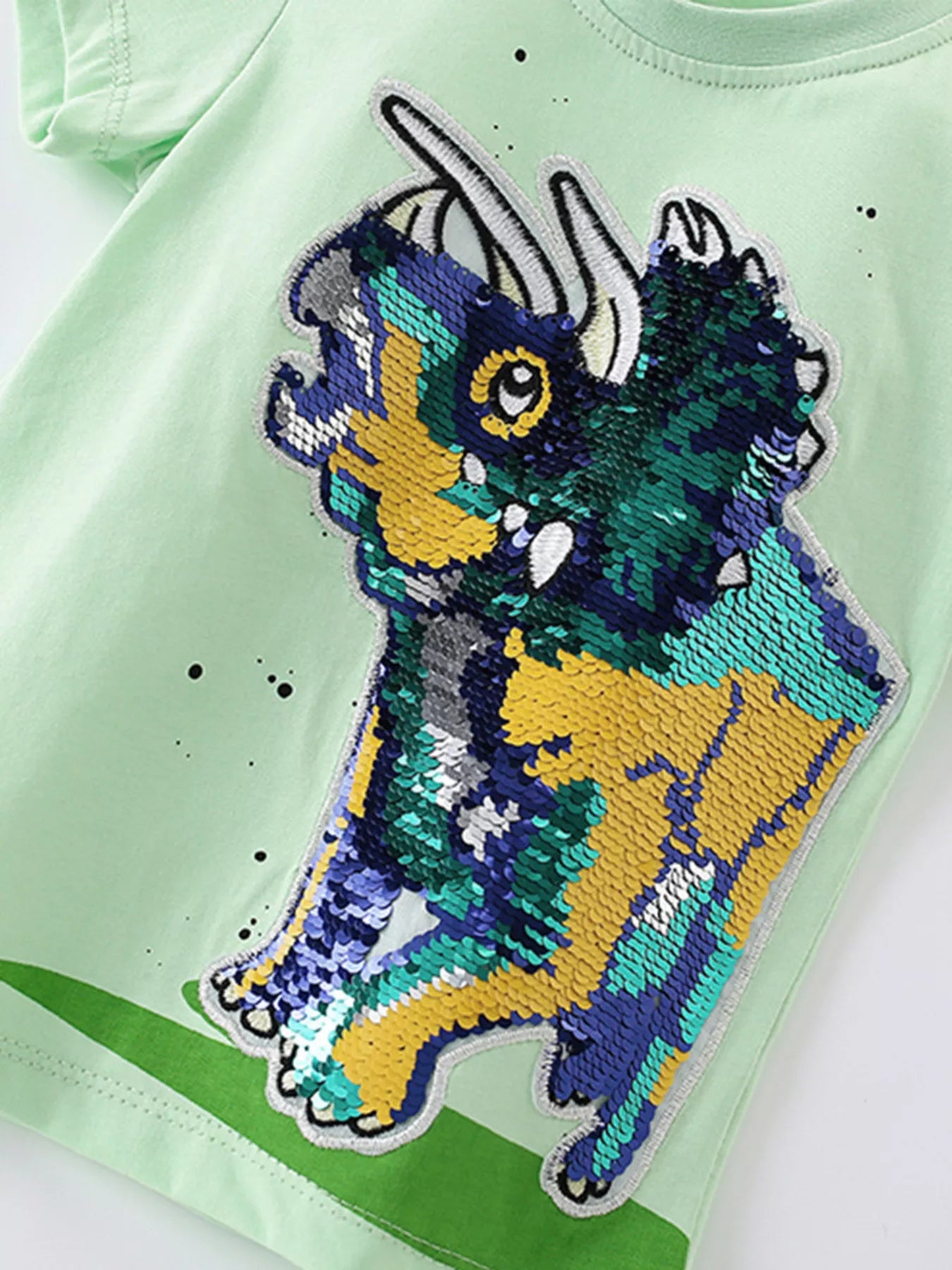 Angled close-up of multicolor sequin dinosaur graphic on light green children's tee