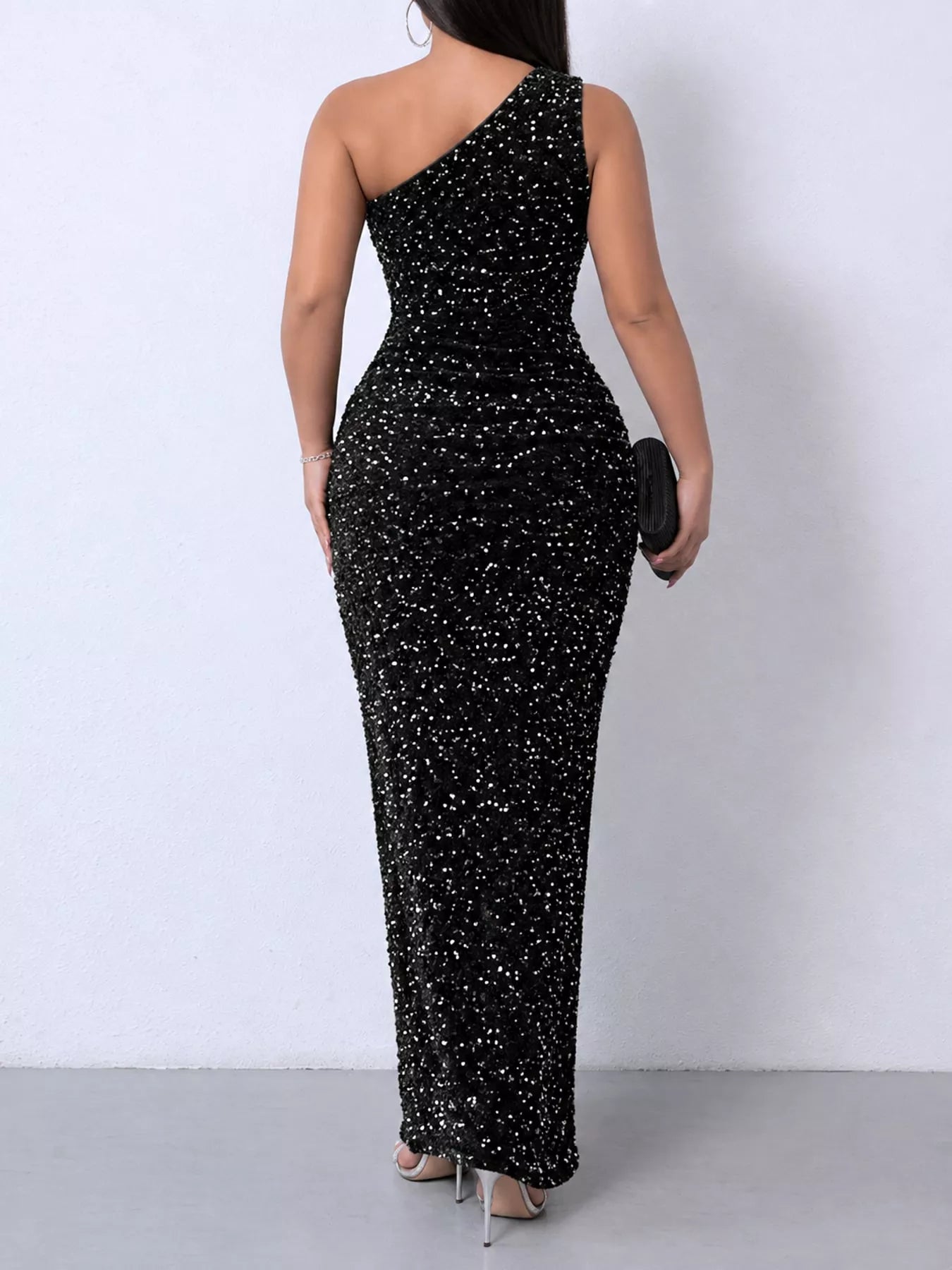 Black sequin one shoulder evening dress worn from the back holding a black clutch