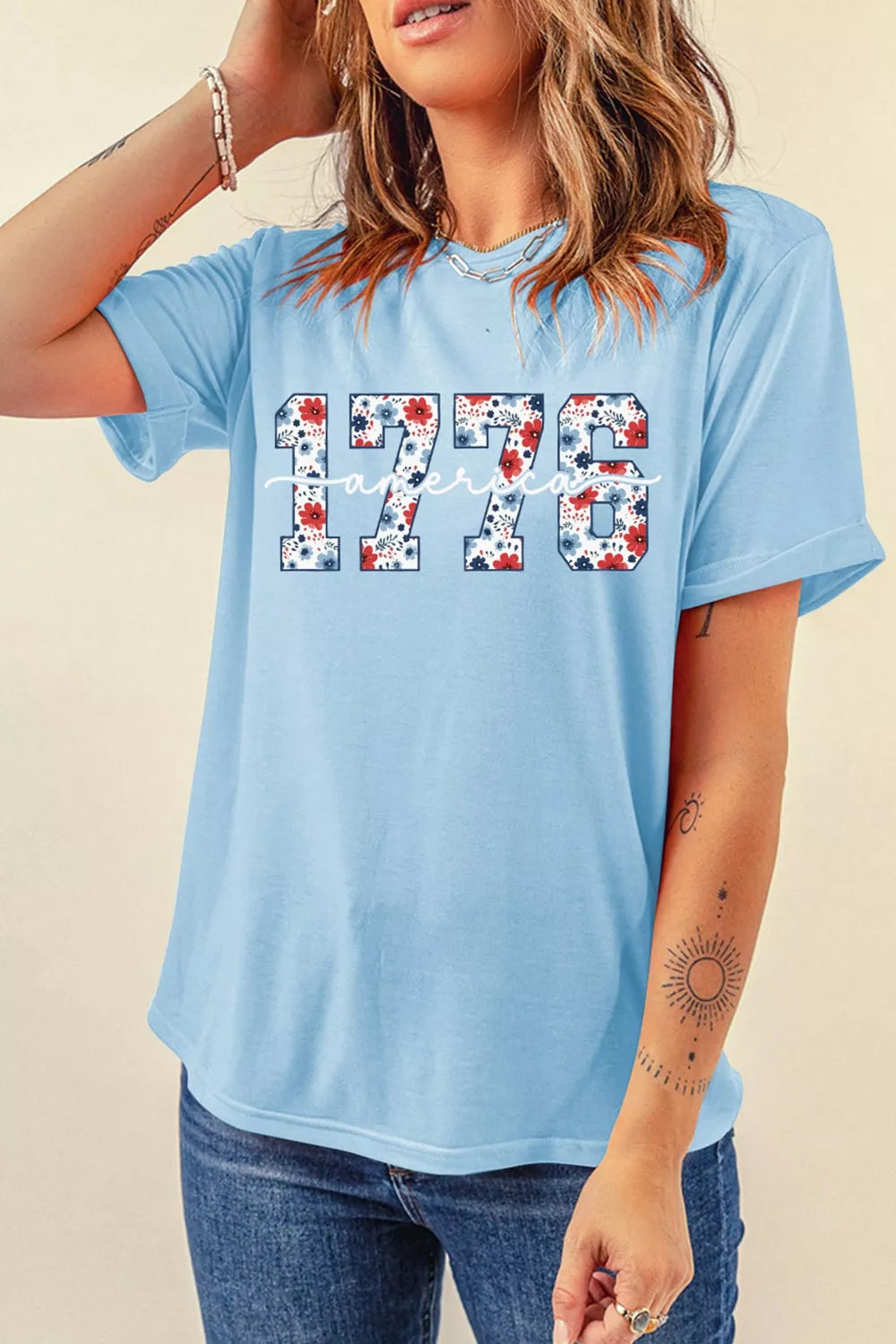 Front view of light blue America 1776 floral print T-shirt modeled with jeans