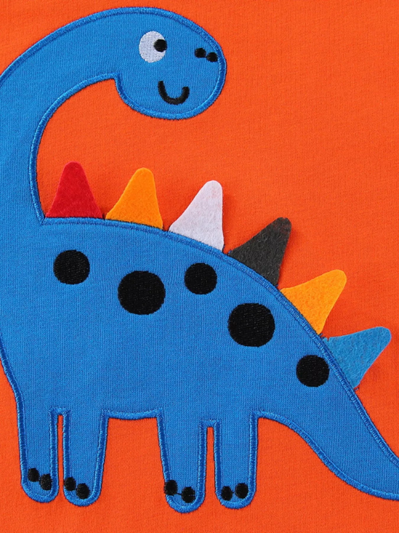 Close view of the blue dinosaur applique with black spots and colourful spikes on orange fabric