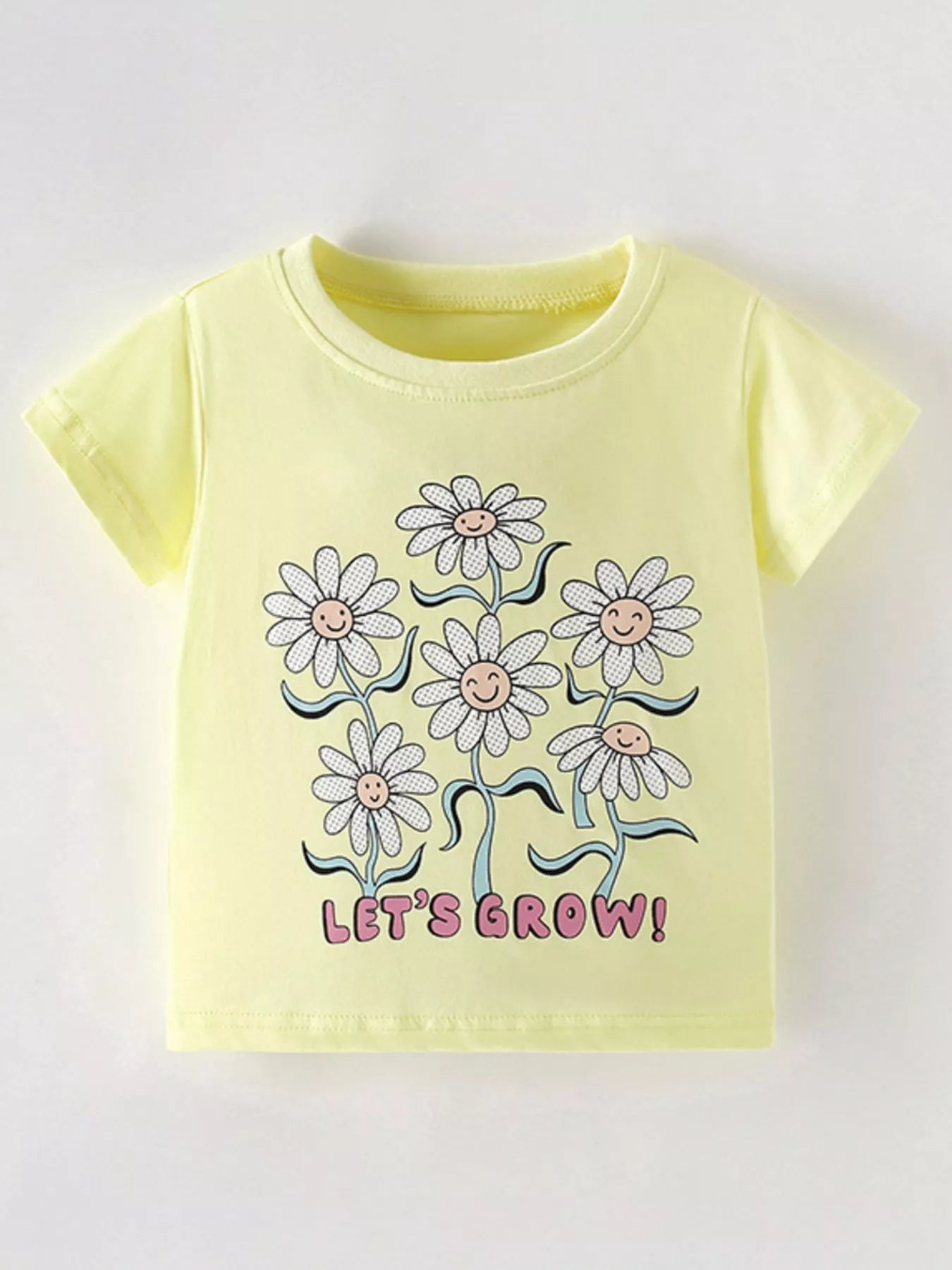 Flat front view of a light yellow children's tee with smiling daisies and pink lettering below