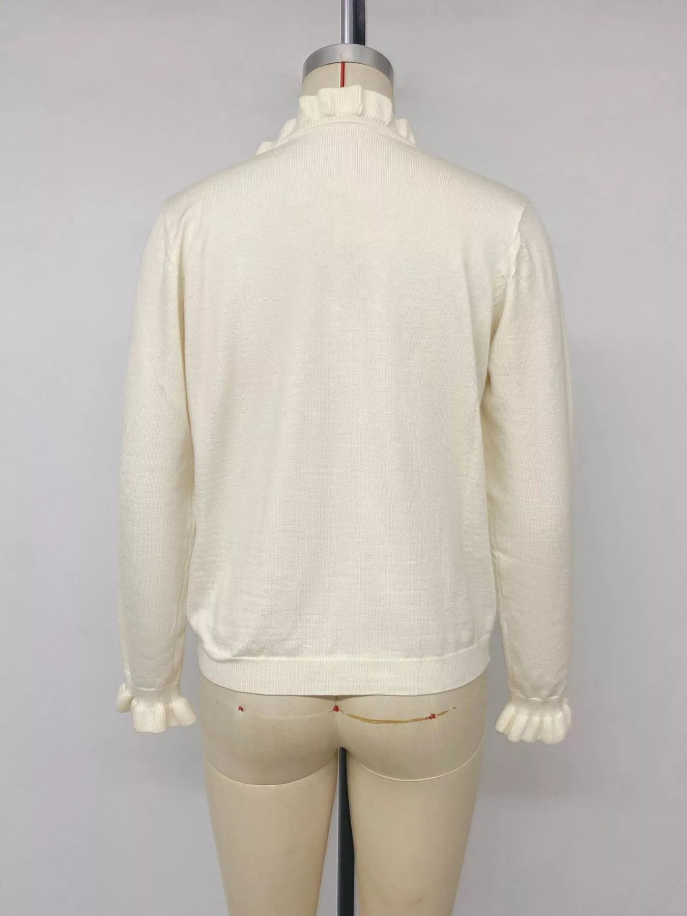 Back view of cream V neck knit top with ruffle cuffs displayed on mannequin