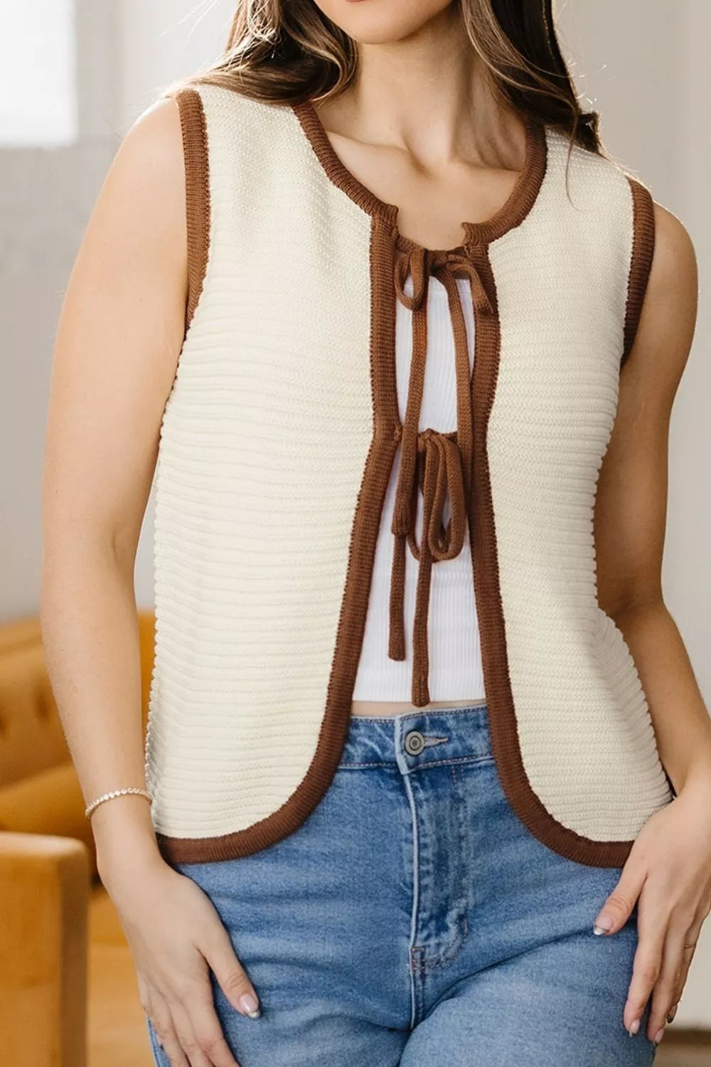 On-model front view of a beige tie front sweater vest with brown trim, hands at sides
