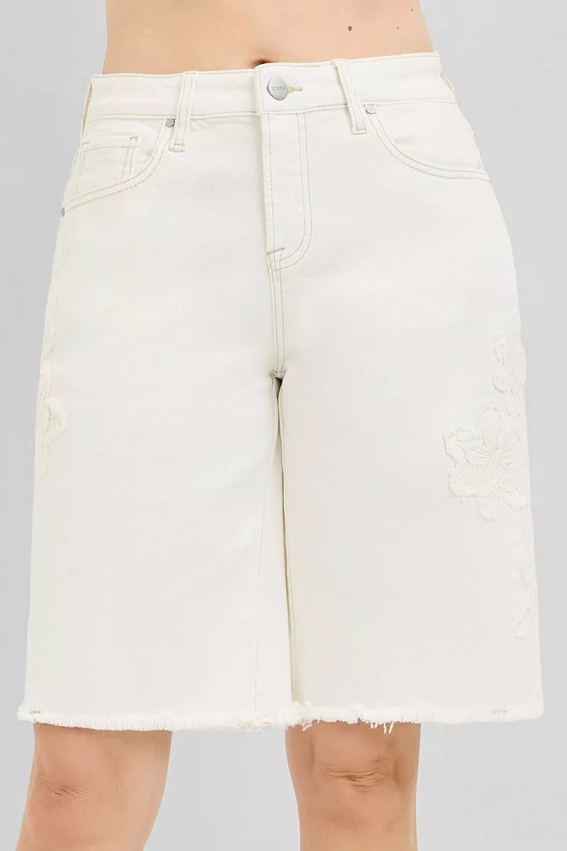 Women's cream Bermuda denim shorts with floral embroidery, raw hems, and a relaxed fit.