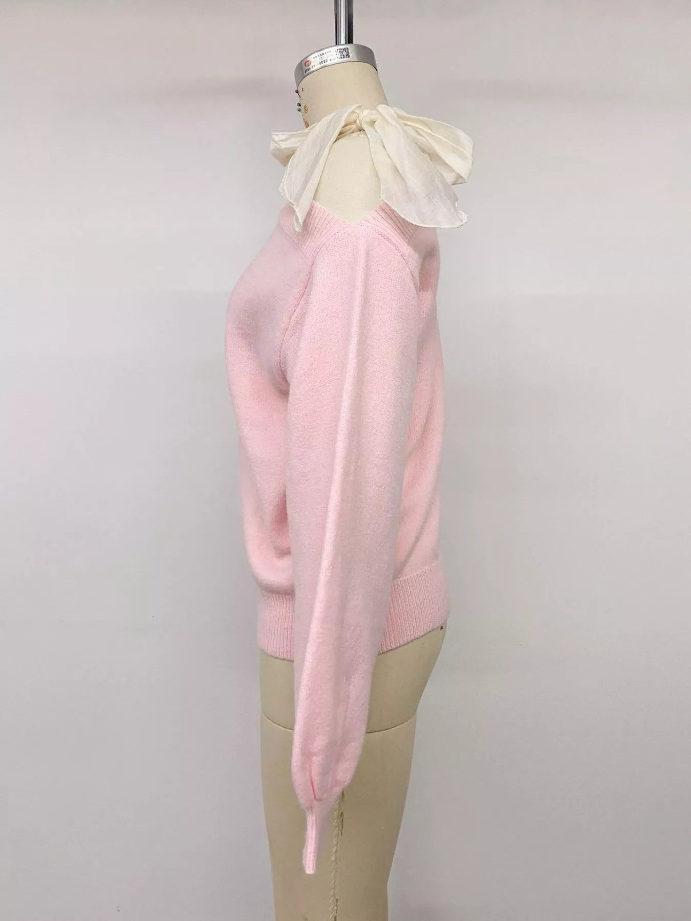Side view of a pink one-shoulder sweater with a cream bow on a mannequin