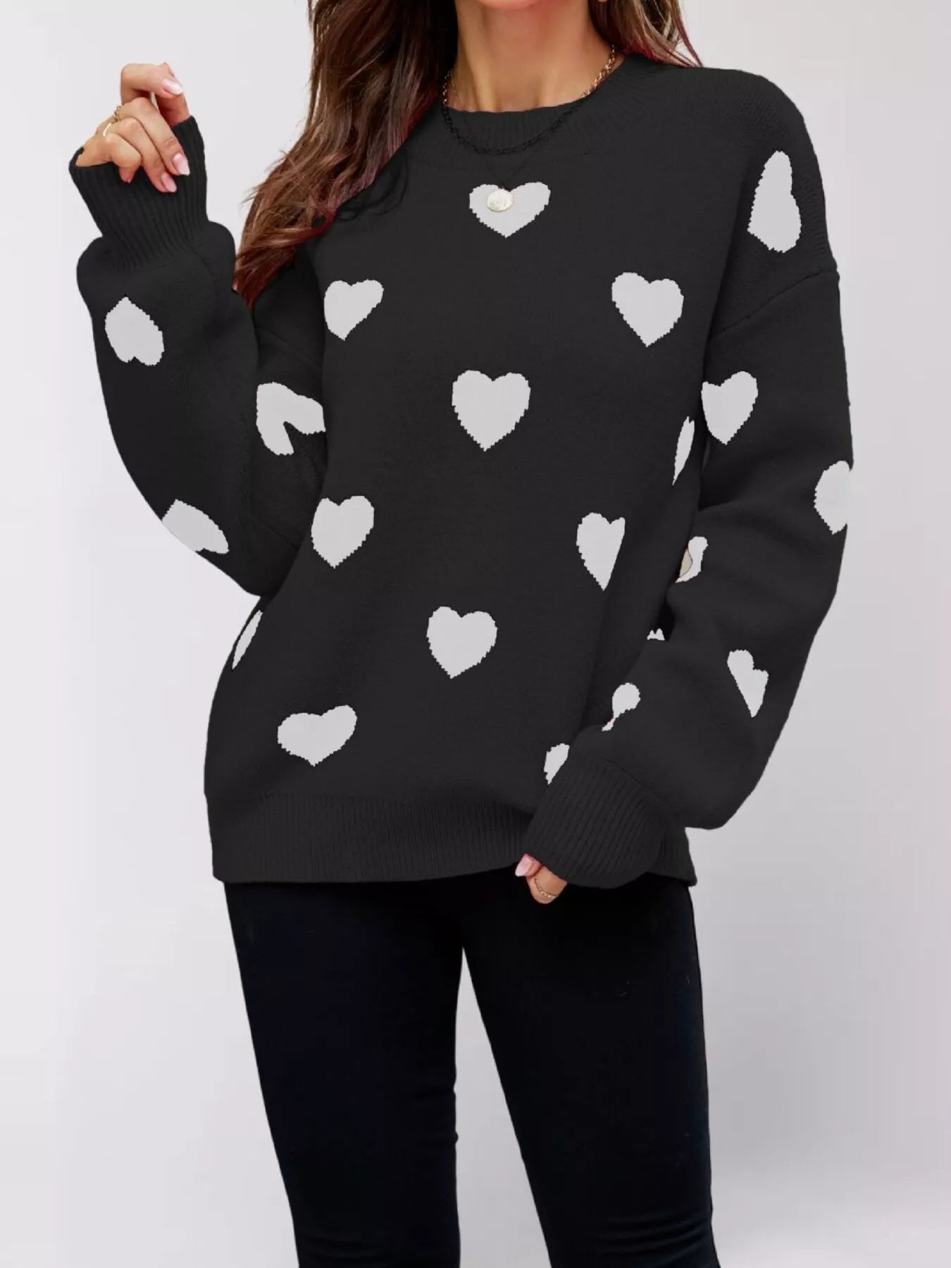 Front view of the black dropped shoulder sweater with white hearts, one arm raised.