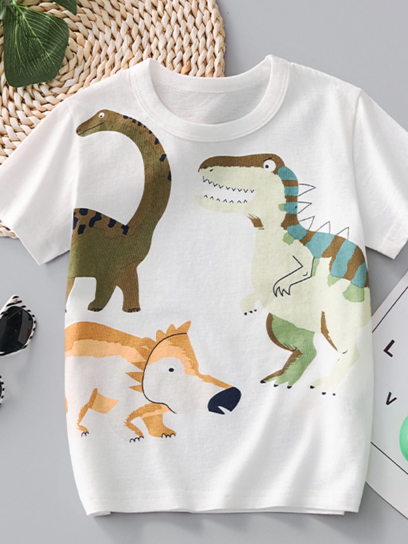 White children's crew neck t-shirt laid flat with large colorful dinosaur print
