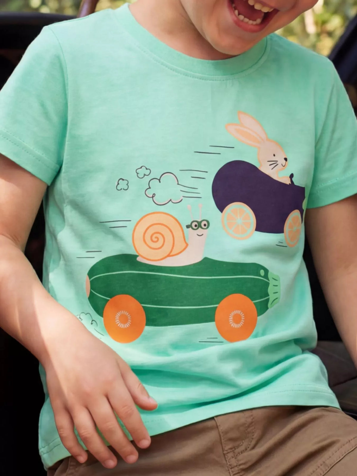 Green children's short sleeve T-shirt shown worn with a snail and bunny racing in vegetable cars