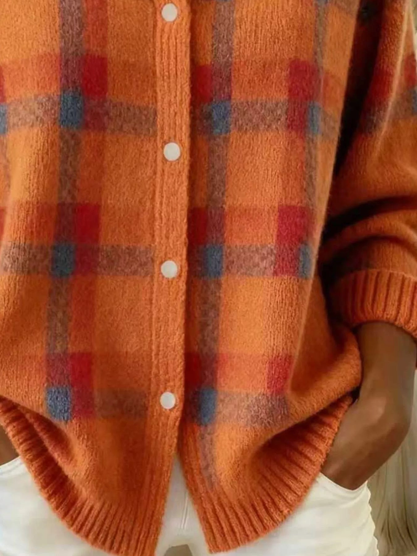 Close-up of the lower front and ribbed hem of an orange and red plaid knit cardigan
