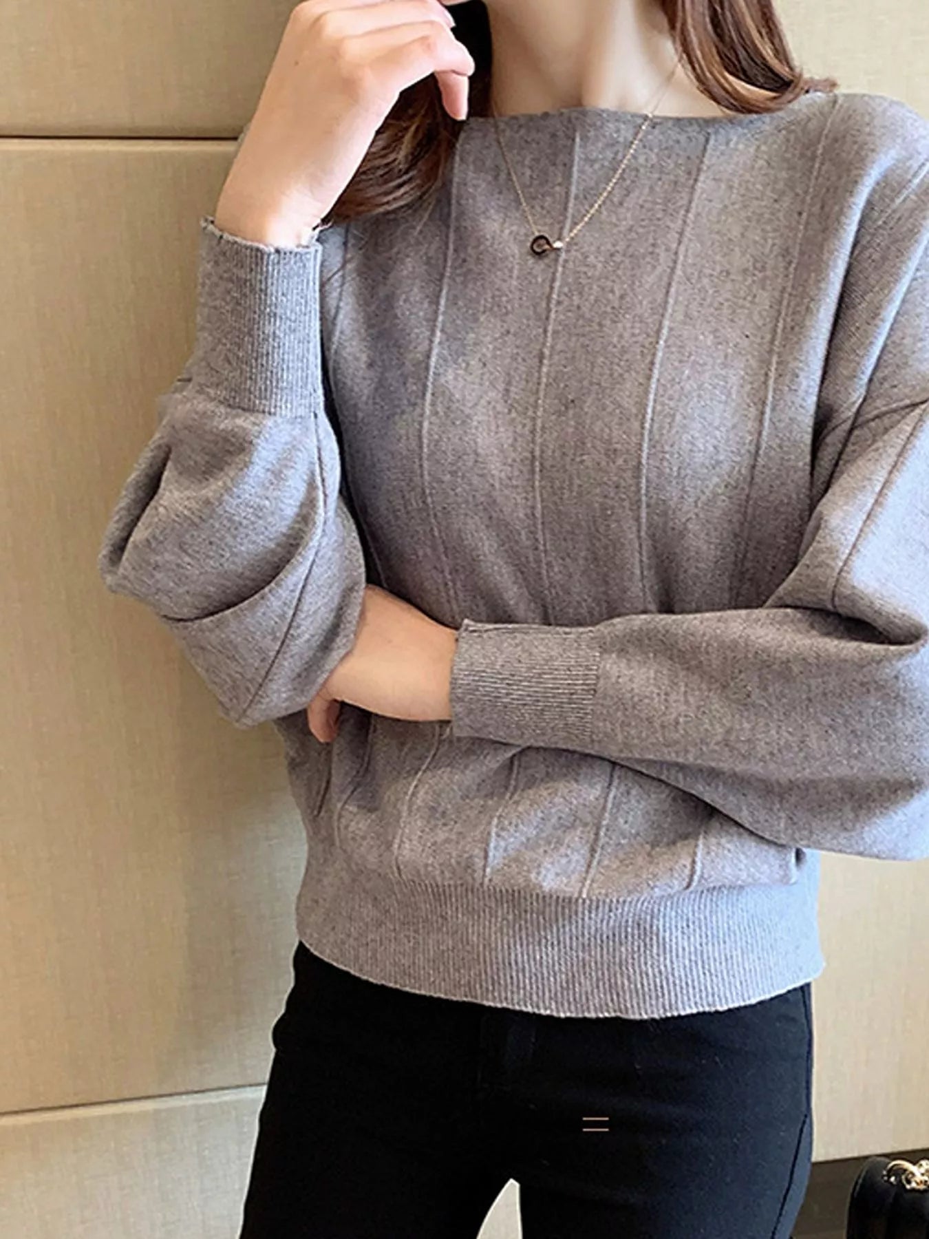 Close front view of the gray batwing sleeve knit top with vertical seams, arms crossed.