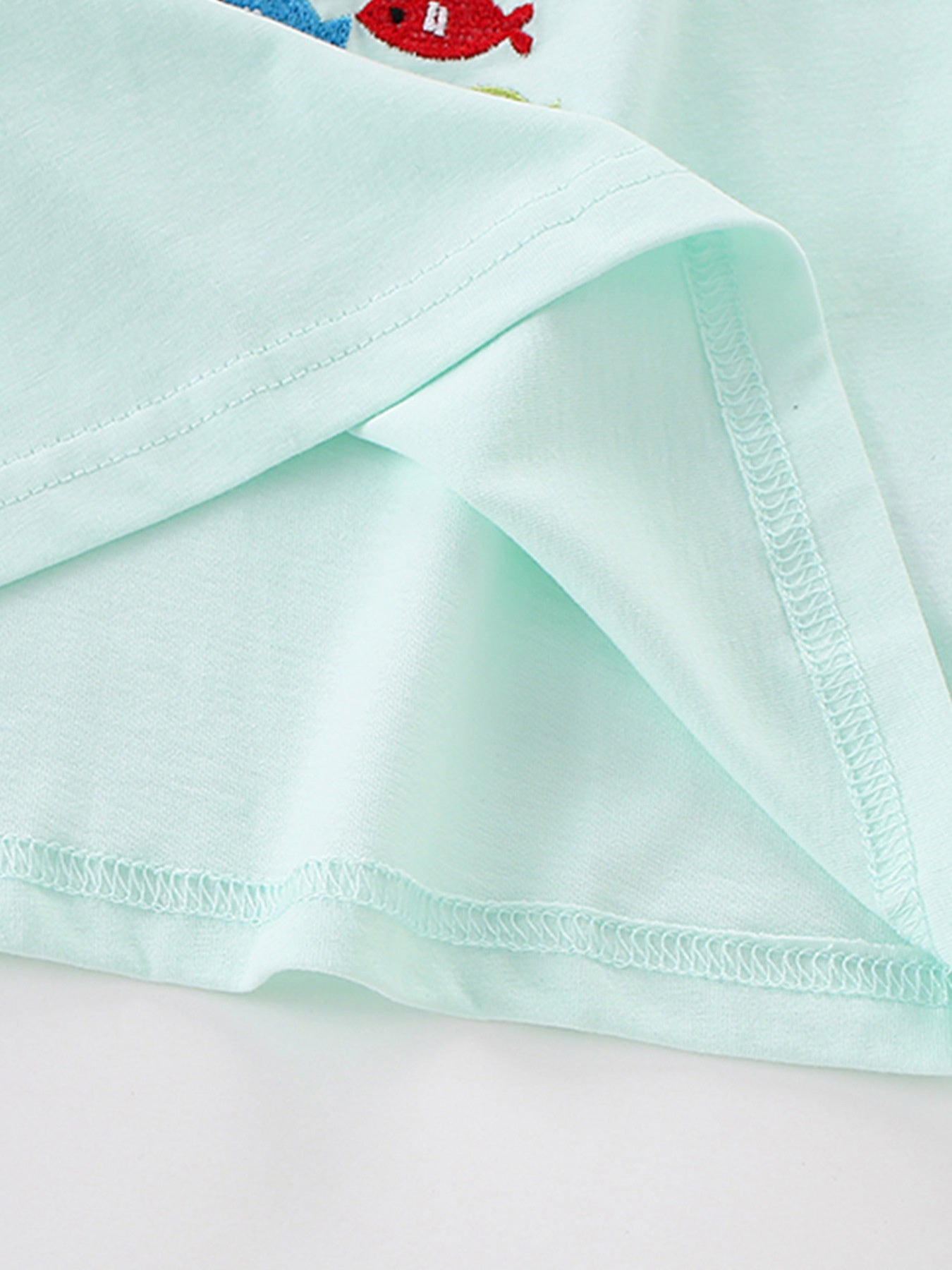 Close view of the mint children's tee hem and sleeve seam showing fine overlock stitching
