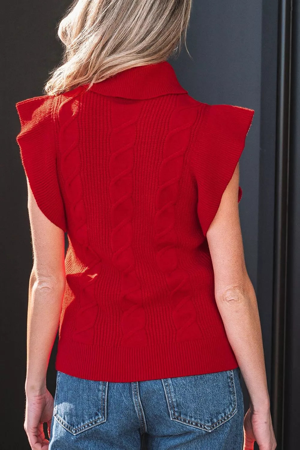 Back view of a red cable knit turtleneck sweater with ruffled short sleeves