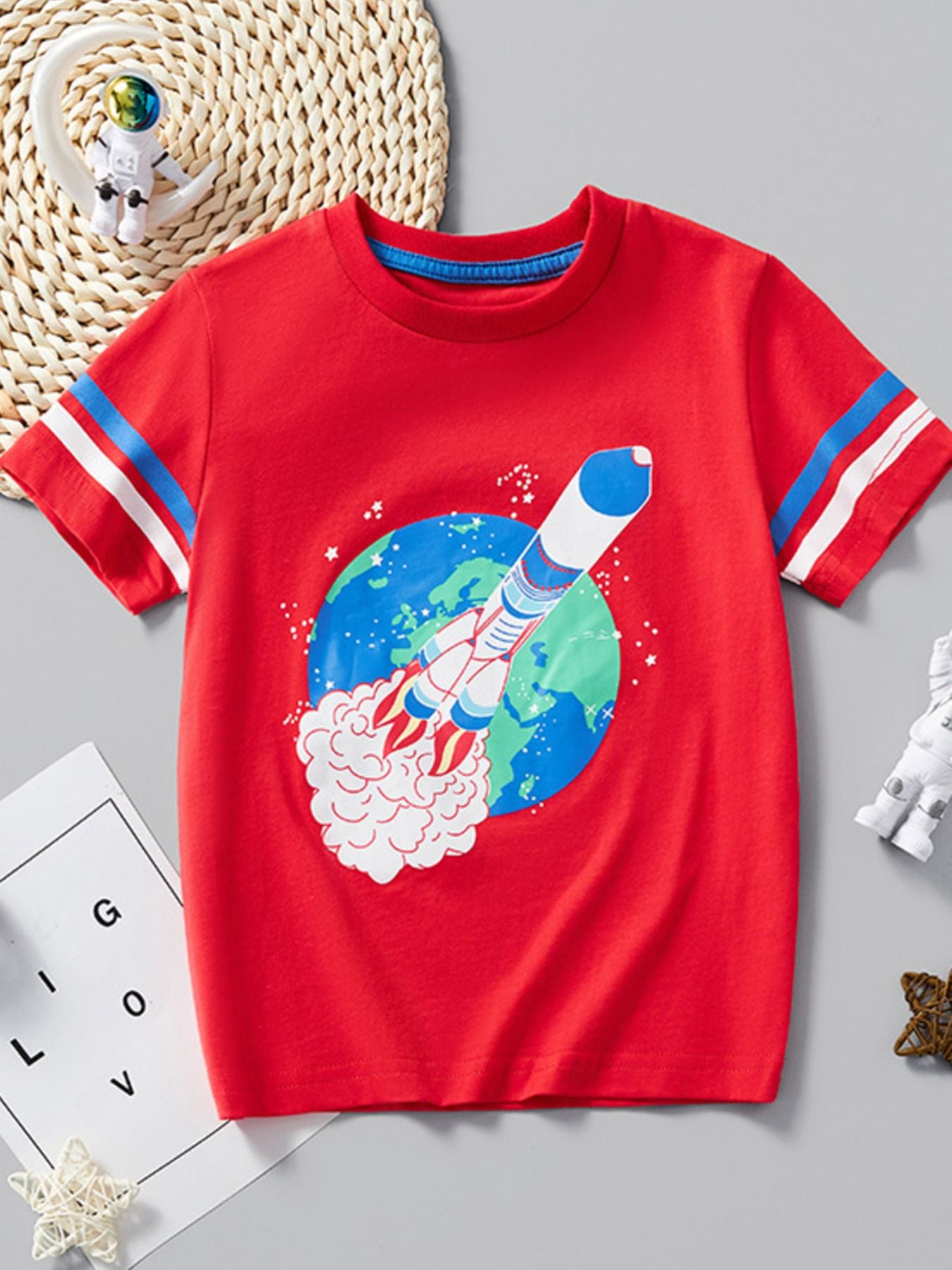 Flat lay front view of red children's T-shirt with a rocket launching past planet Earth
