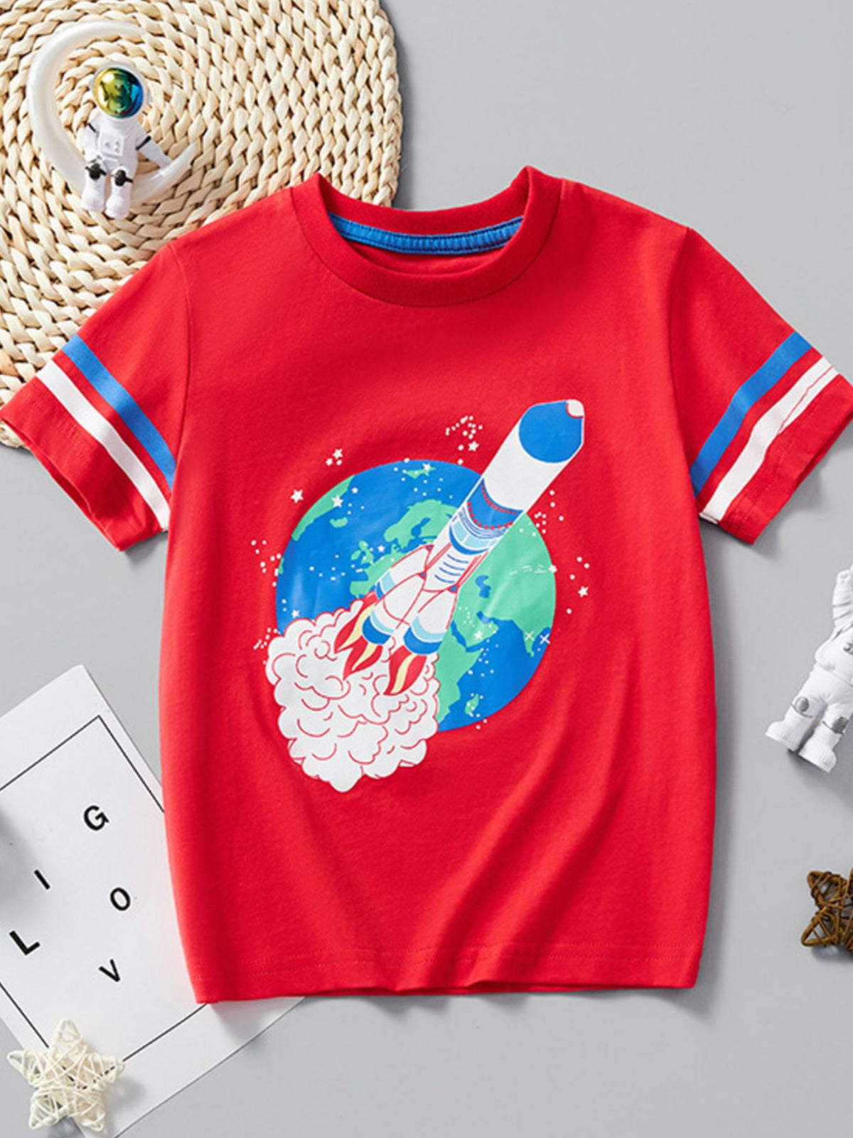 Flat lay front view of red children's T-shirt with a rocket launching past planet Earth
