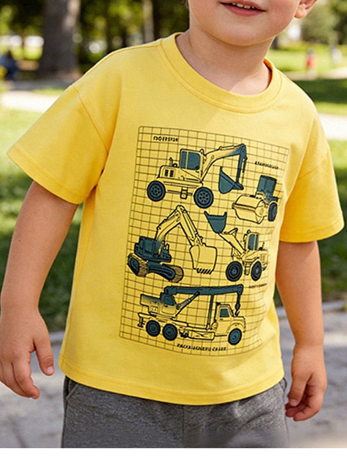 Yellow children's short sleeve t-shirt with excavators, a steamroller, and a crane truck, shown worn outdoors