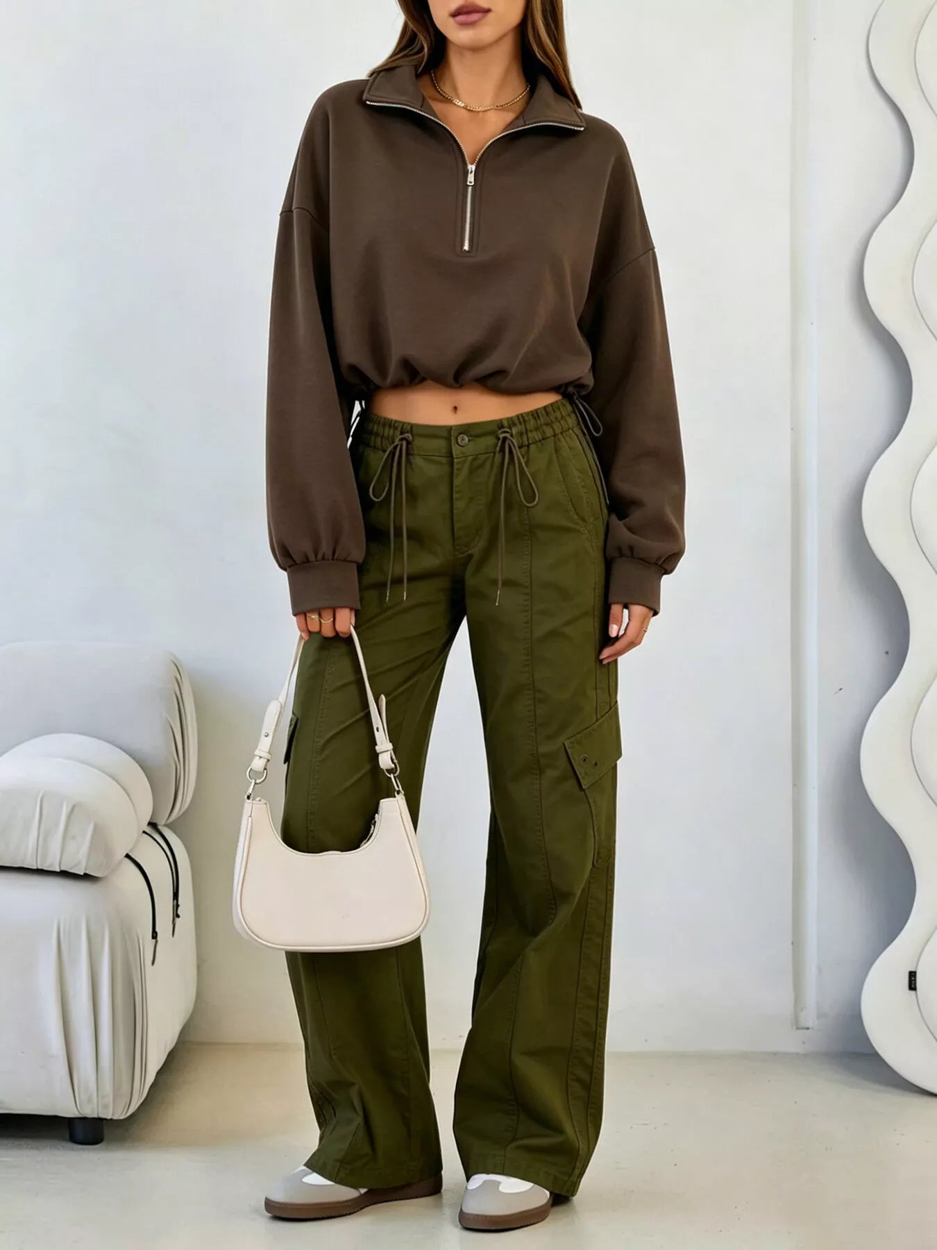 Full length angled view of brown half zip sweatshirt with olive cargo trousers and shoulder bag