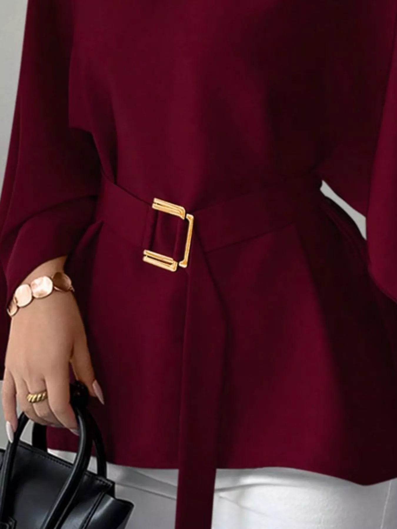 Close detail of burgundy batwing sleeve blouse gold buckle belt and flared hem