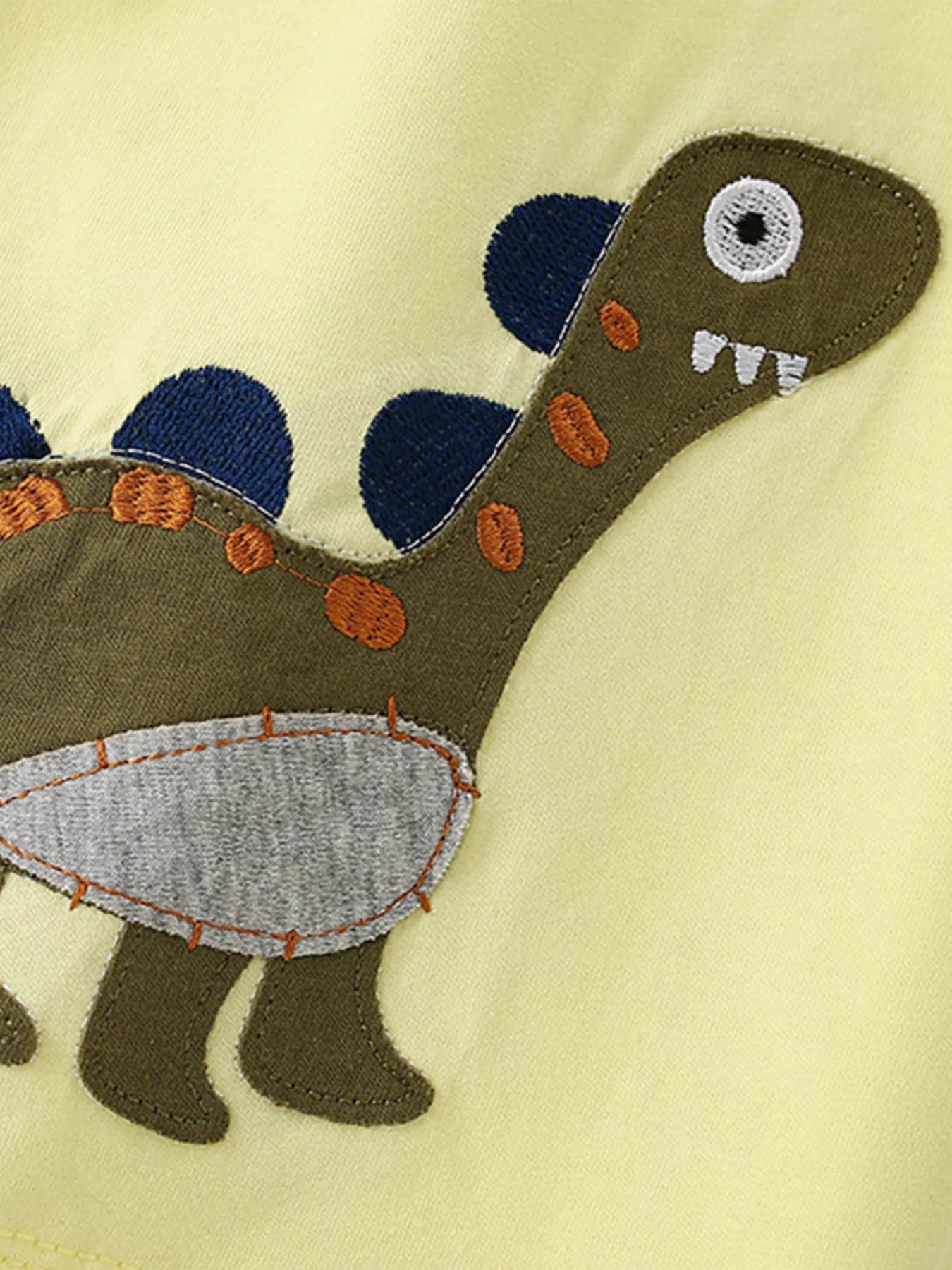 Close-up detail of the green dinosaur applique with blue spikes and orange stitching