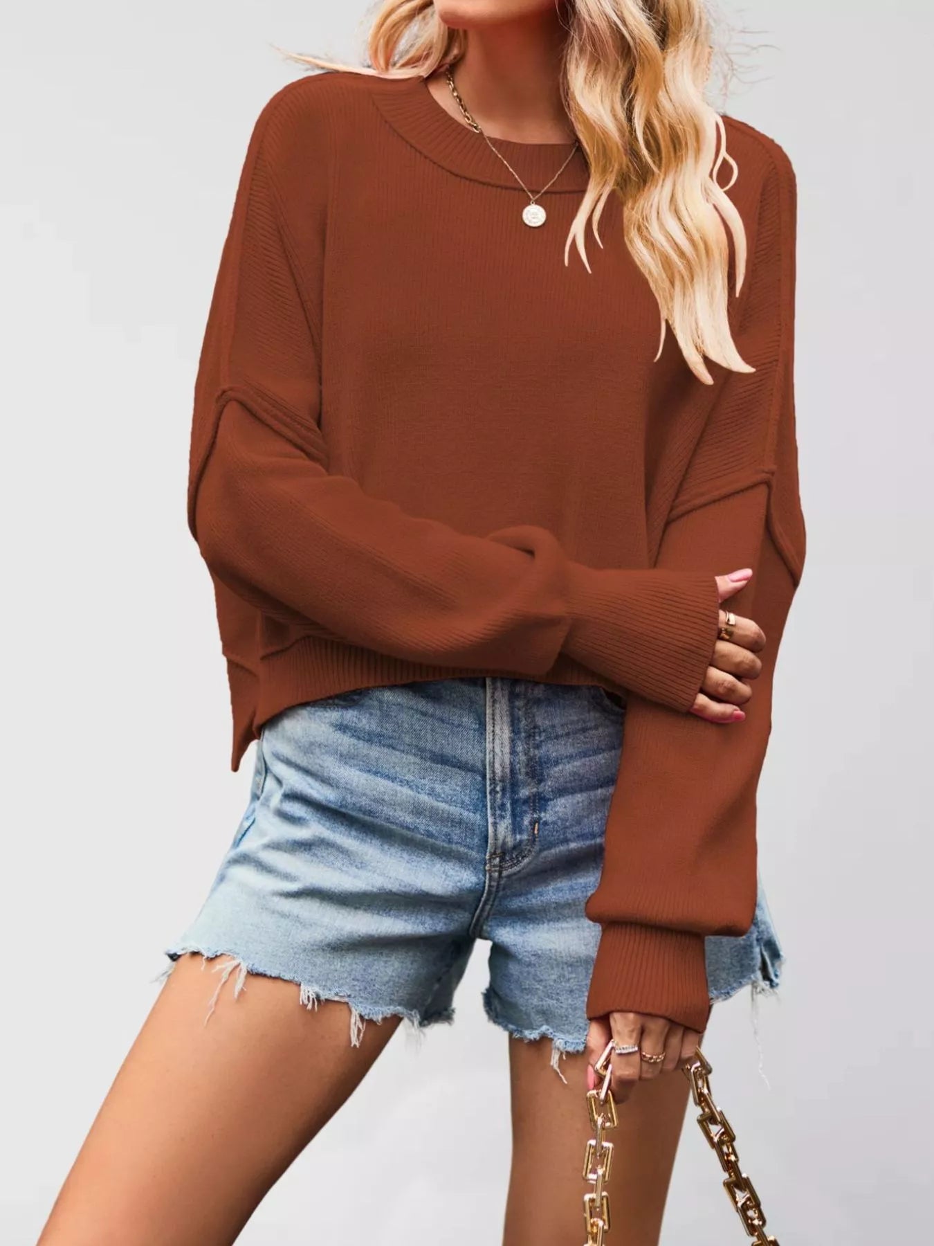 Front view of a rust brown crew neck dropped shoulder sweater with ribbed cuffs worn with denim shorts.